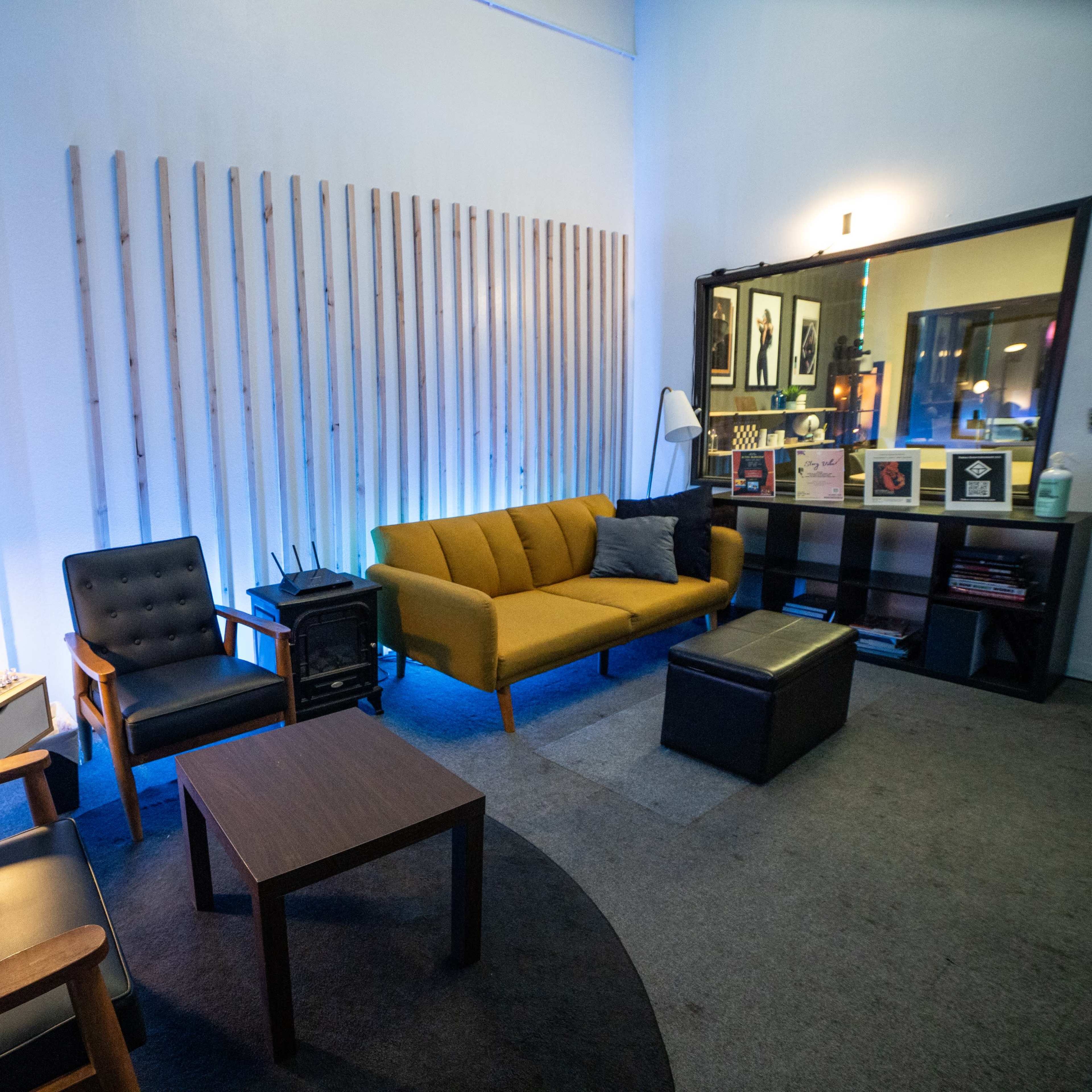 A modern lounge area with yellow and black seating, a small coffee table, and decorative wooden wall panels illuminated by blue lighting.