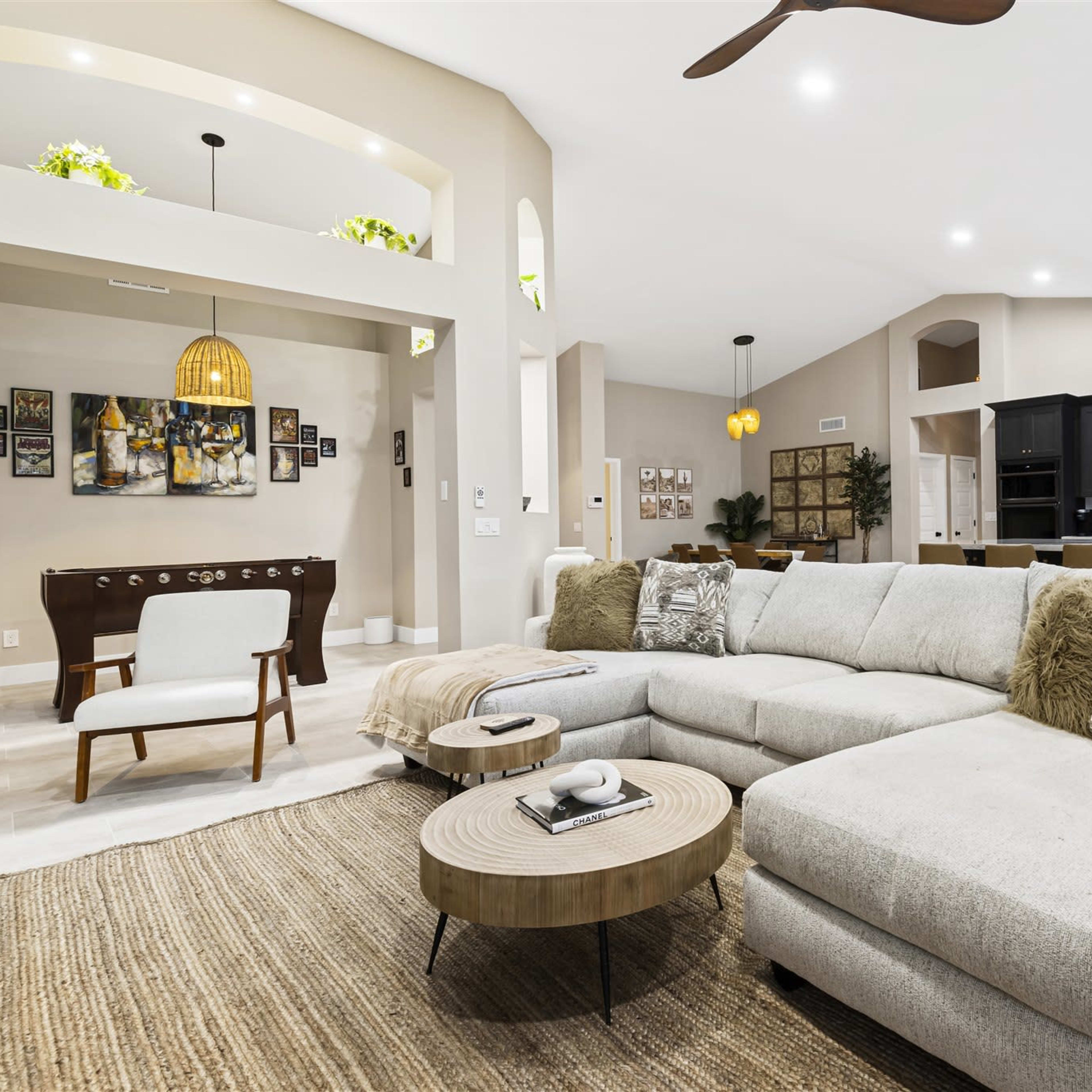 A spacious living area with a light-colored sectional sofa, a round coffee table, and a view of a modern kitchen in the background.