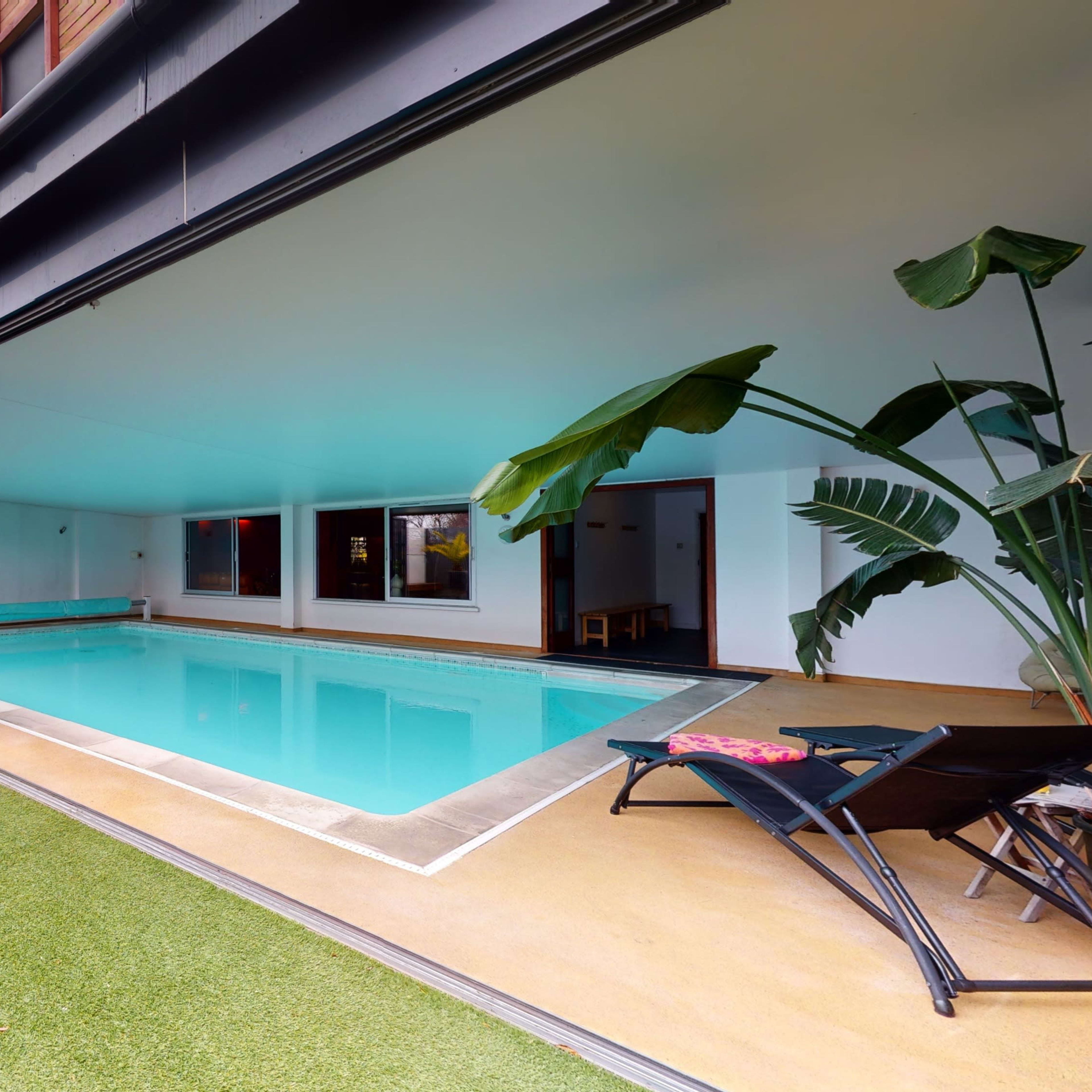 A modern indoor swimming pool surrounded by sliding glass doors and a well-maintained lawn area.