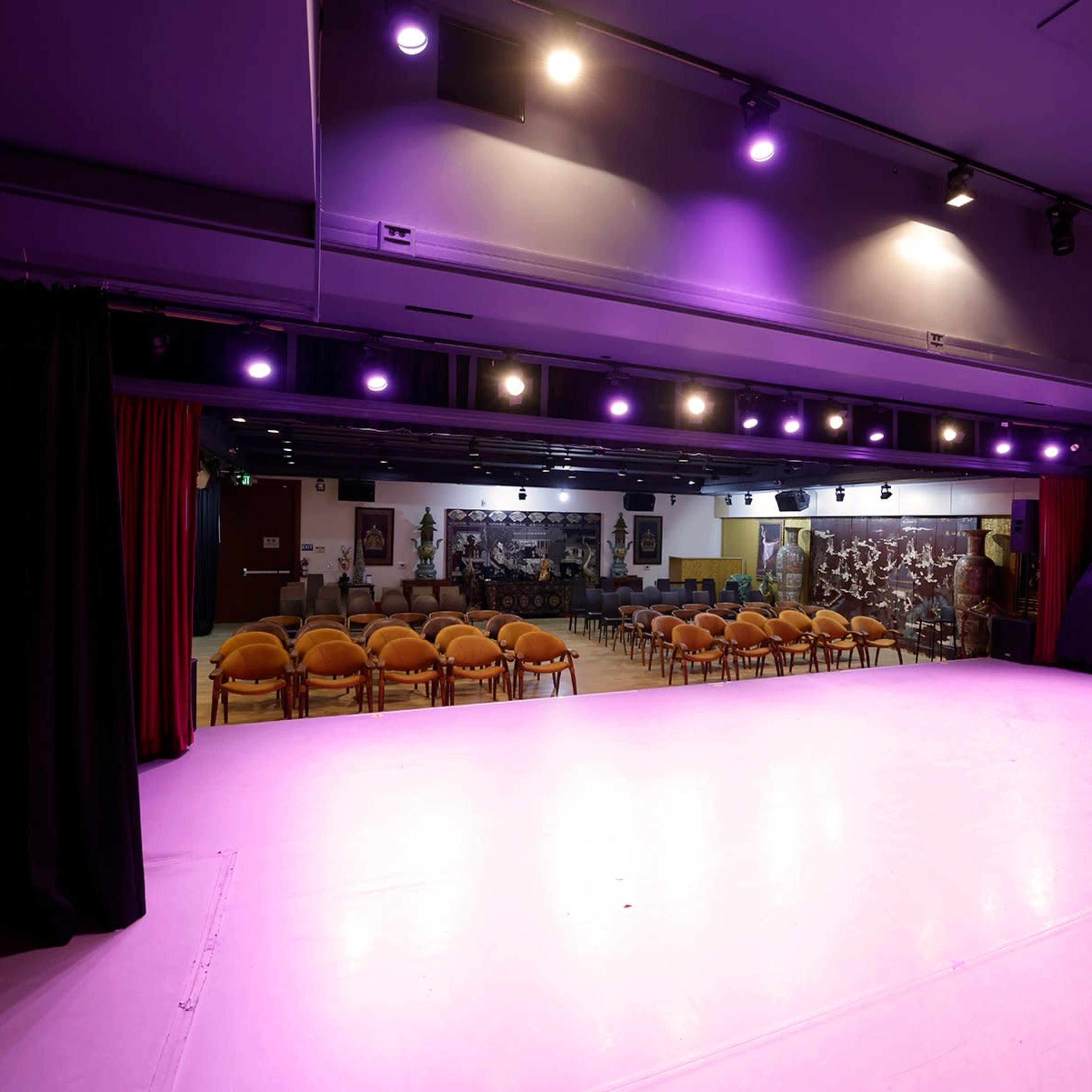 A stage area with bright lights and a seating arrangement of orange chairs facing it.