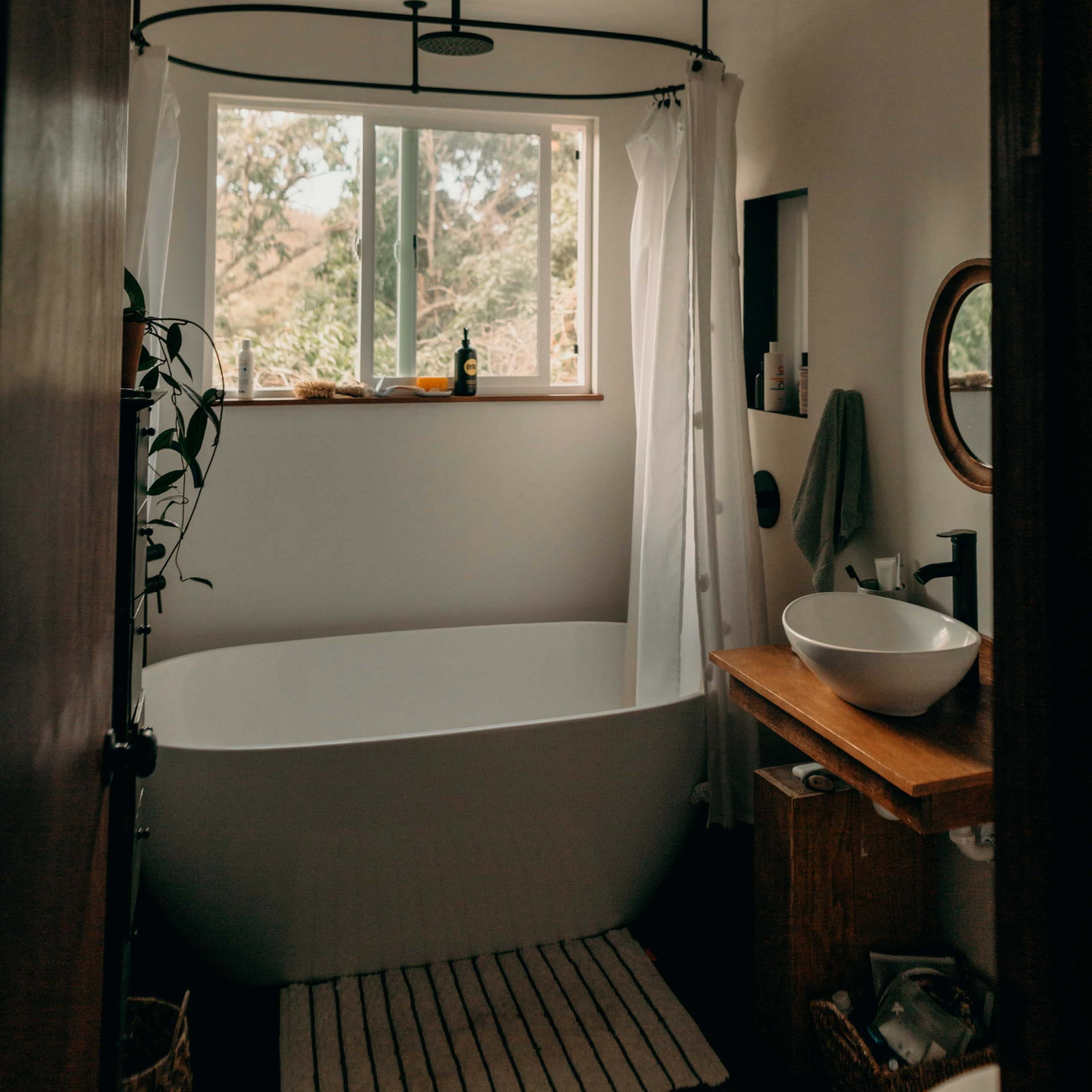A bright bathroom featuring a freestanding bathtub, a window with views, and a wooden vanity.