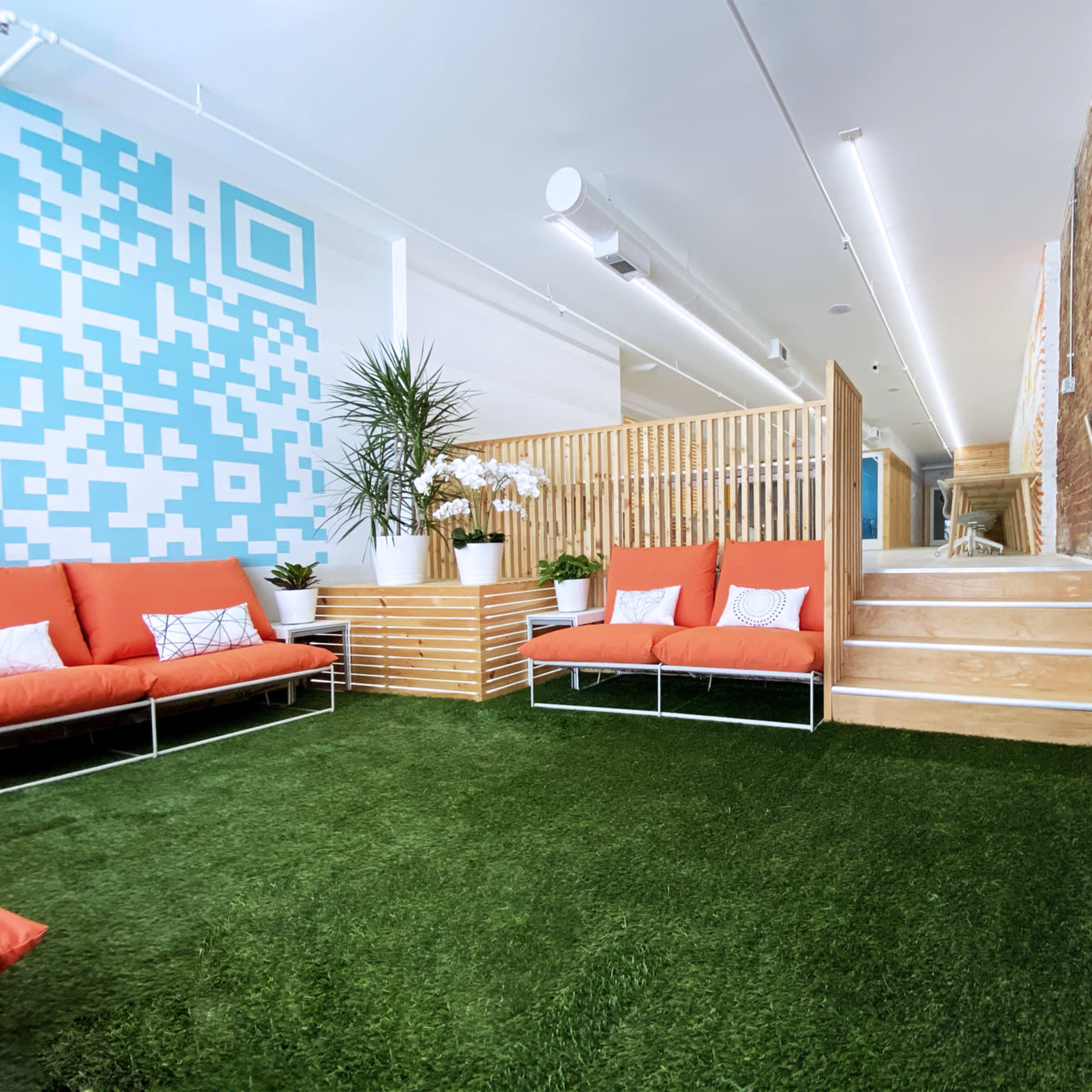 A modern interior space with orange couches, green artificial grass flooring, and a wooden partition separating different areas.