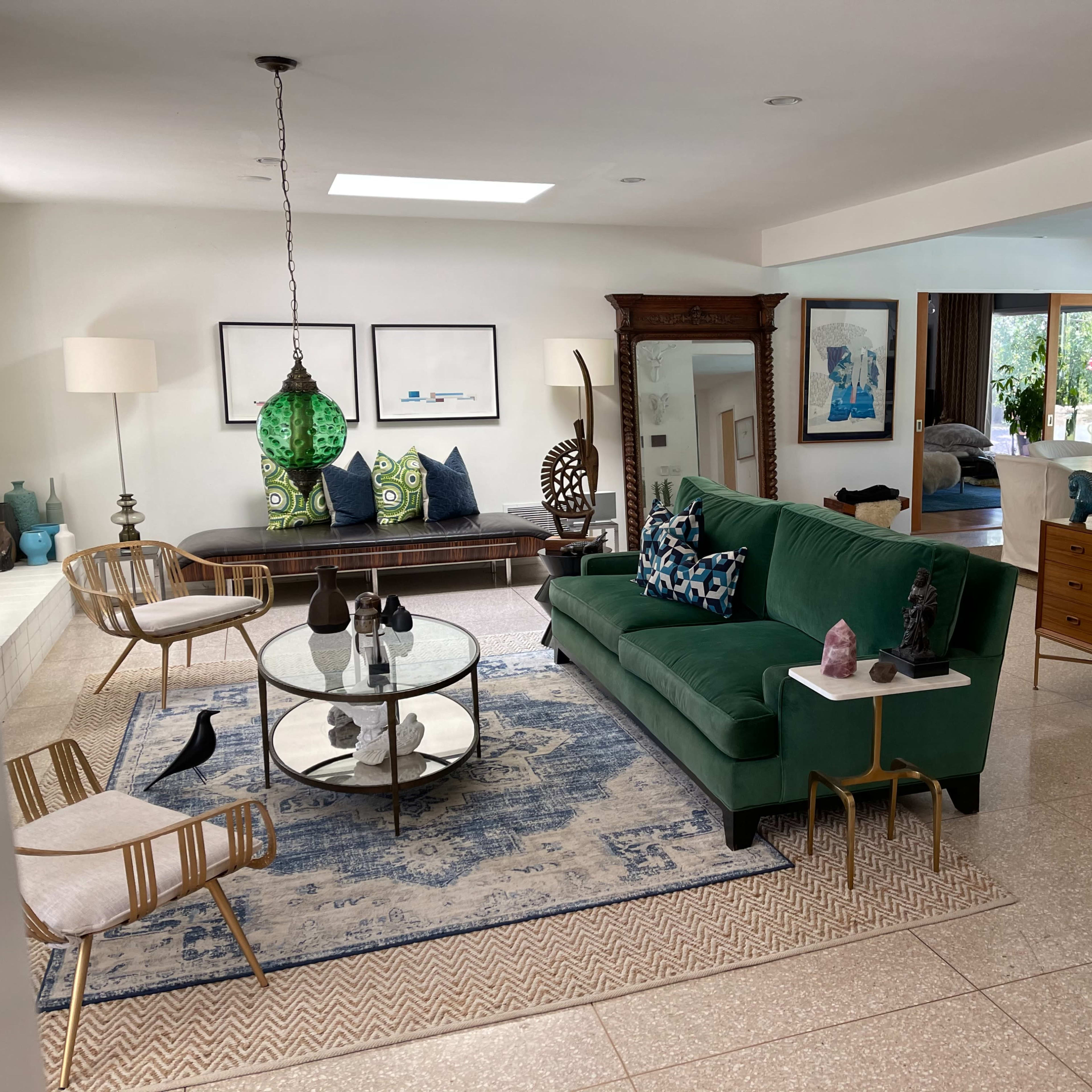 A spacious living room with a green sofa, glass coffee table, decorative furnishings, and an open layout connecting to other areas.