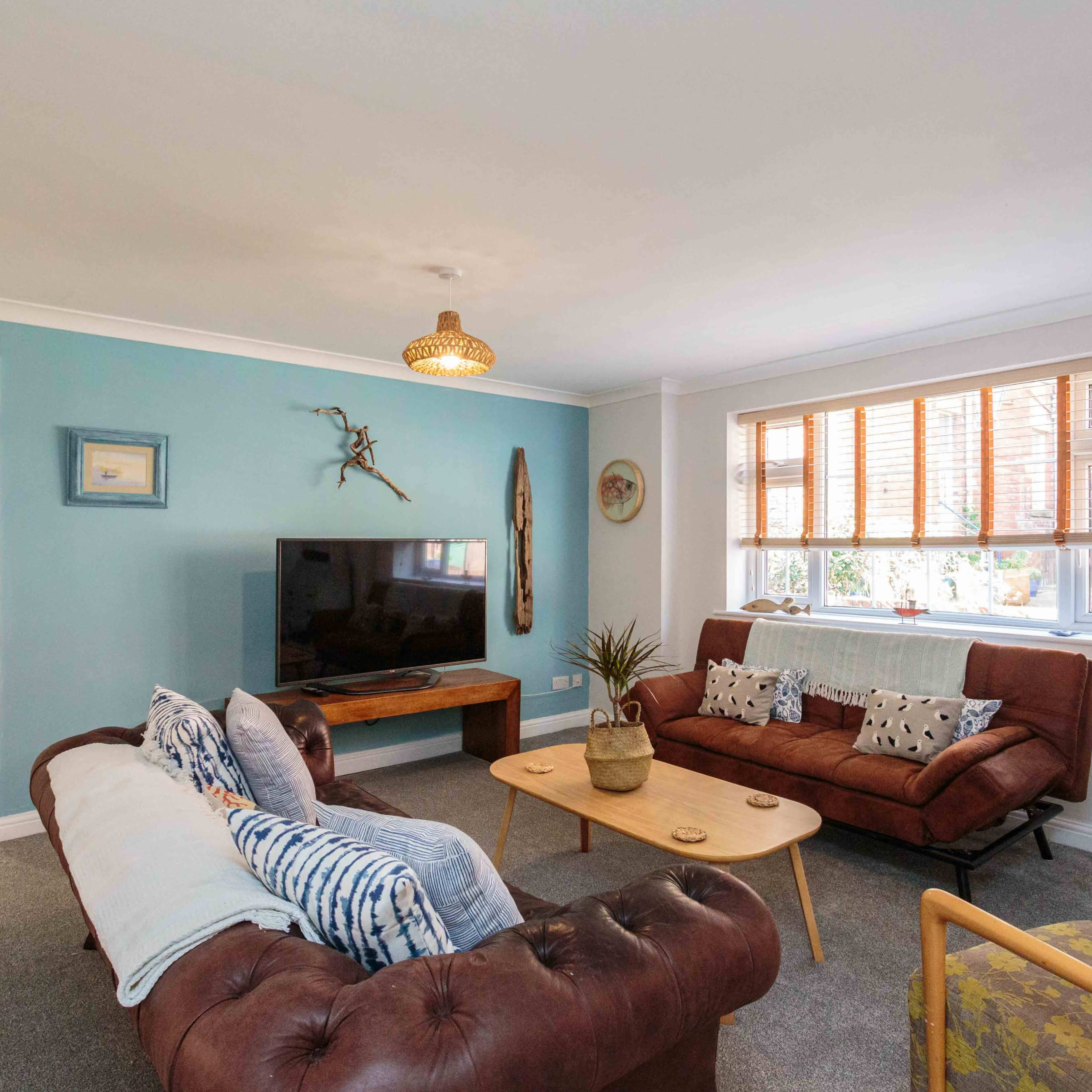 A modern living room features a television, a wooden coffee table, brown leather sofas, and a decorative wall.