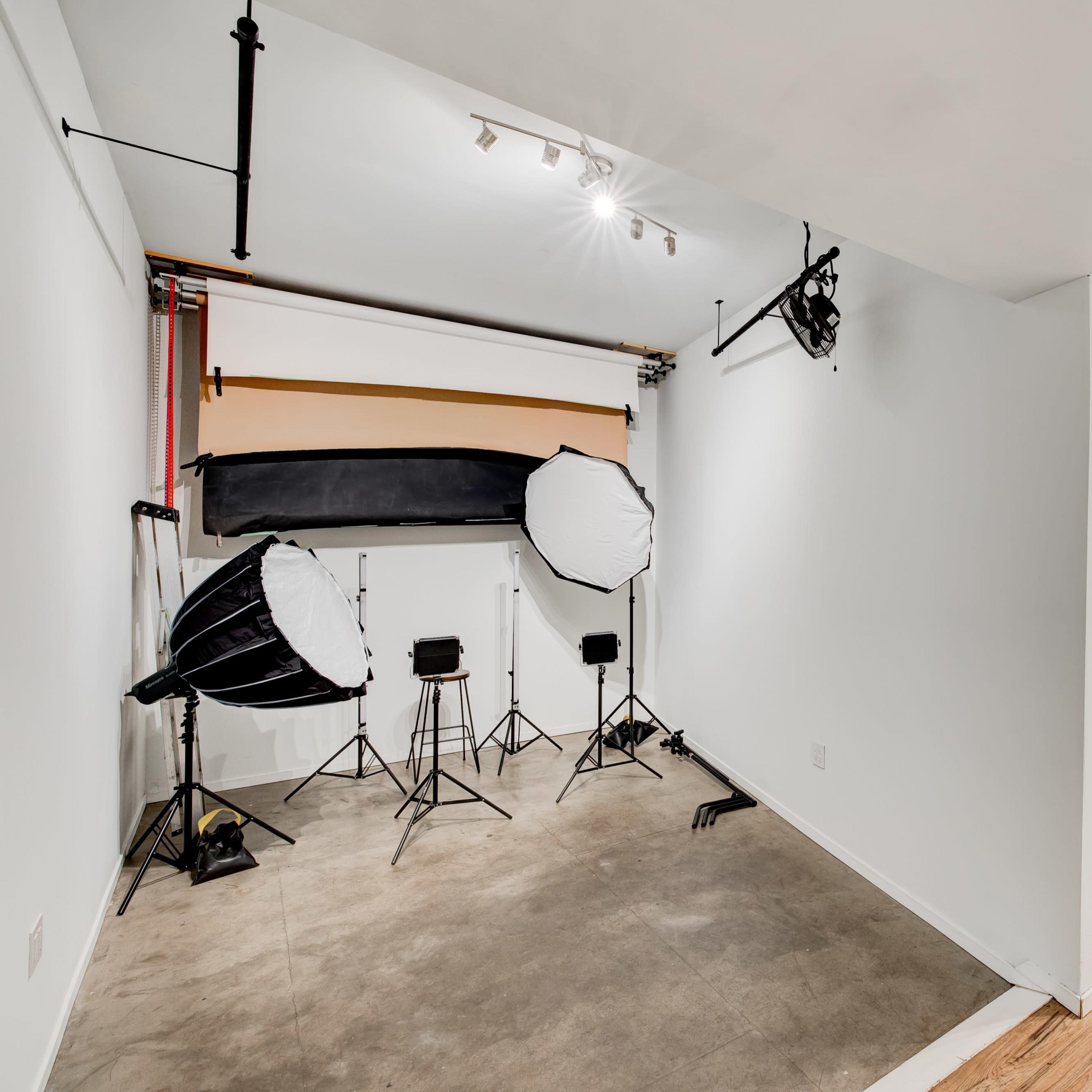 A photography studio with two large softbox lights, a backdrop setup, and a wooden door leading to an adjacent room.