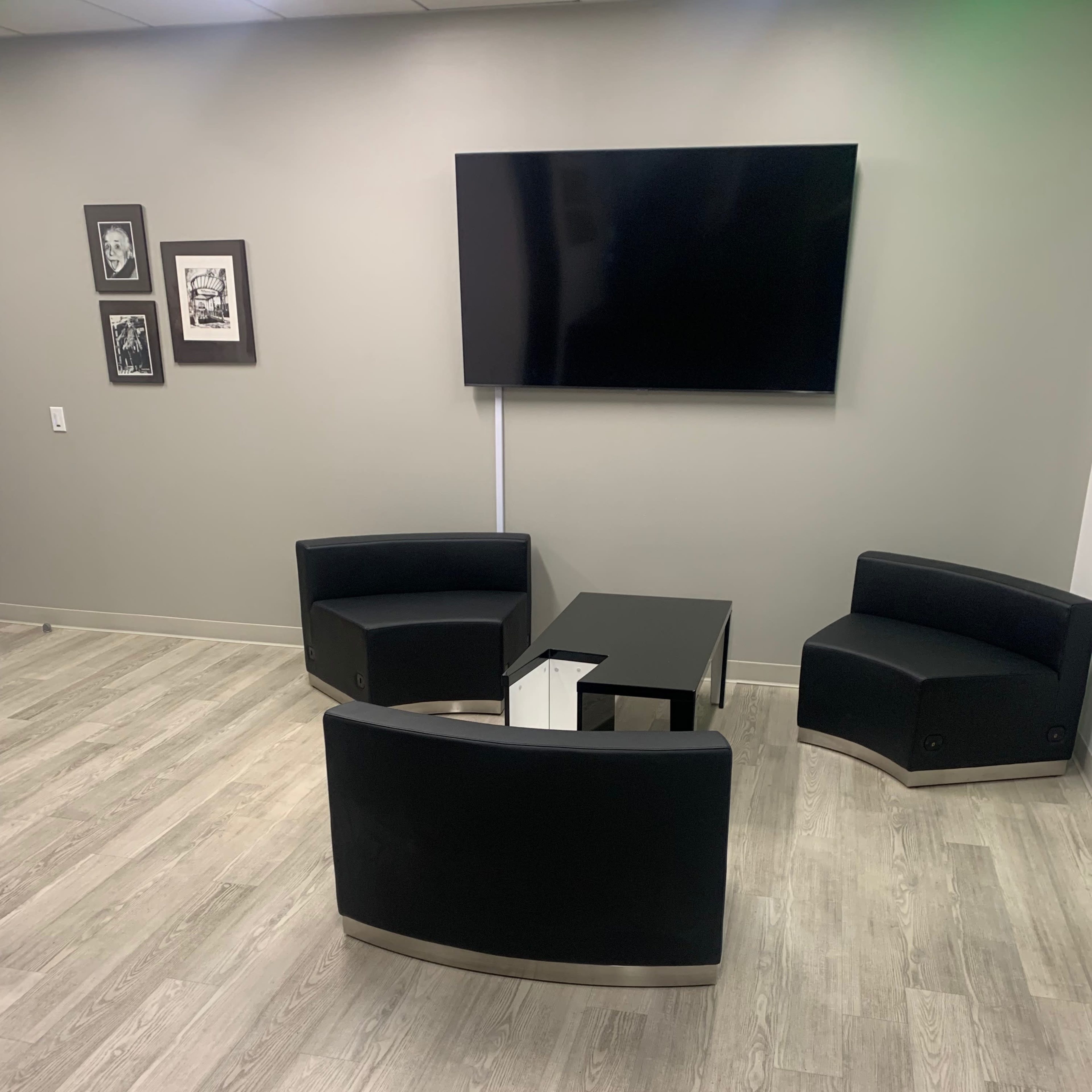 A modern seating area with two curved black chairs and a black coffee table, positioned on a light wooden floor under a wall-mounted television.