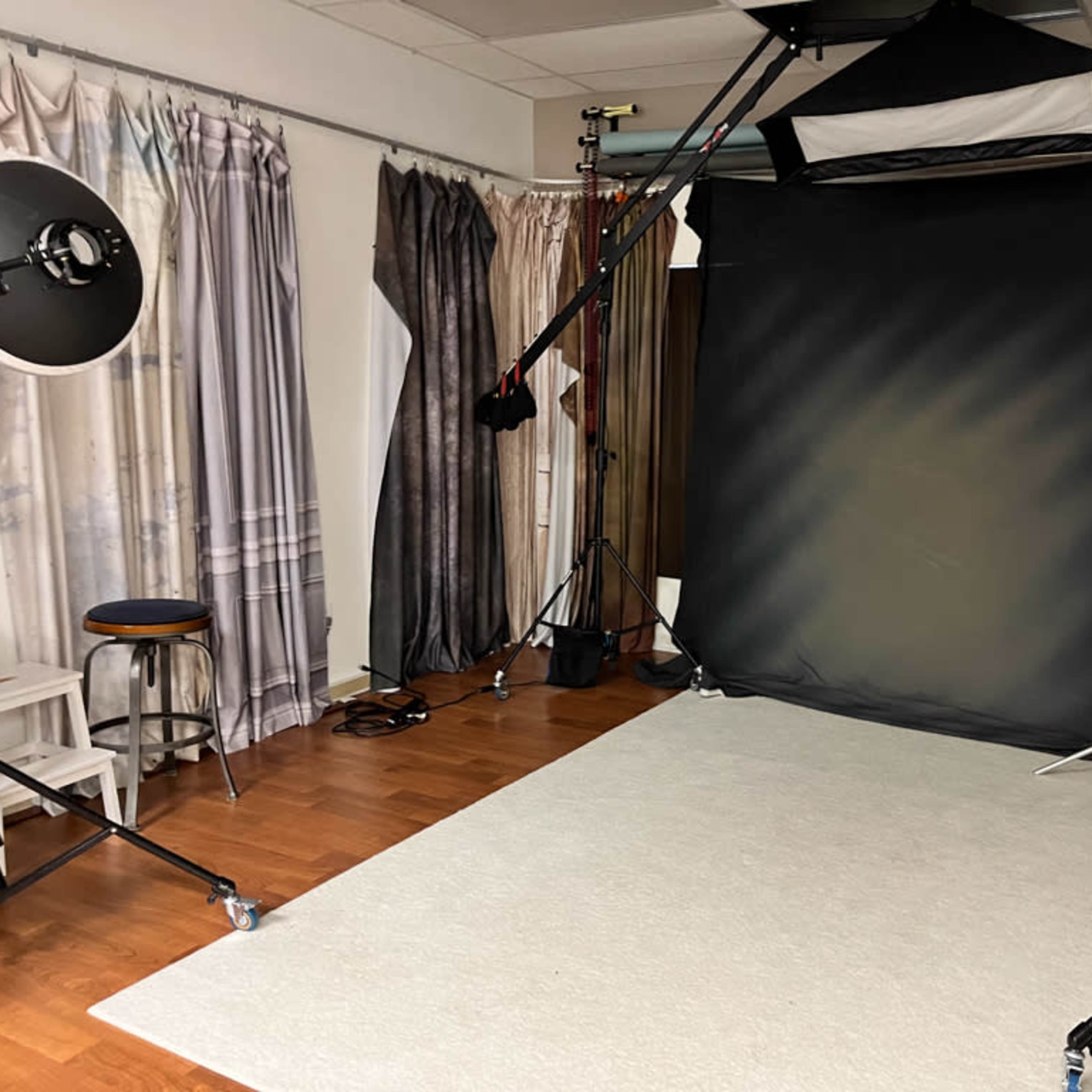 A photography studio with a black backdrop, softbox lighting, and seating arranged on a wooden floor.
