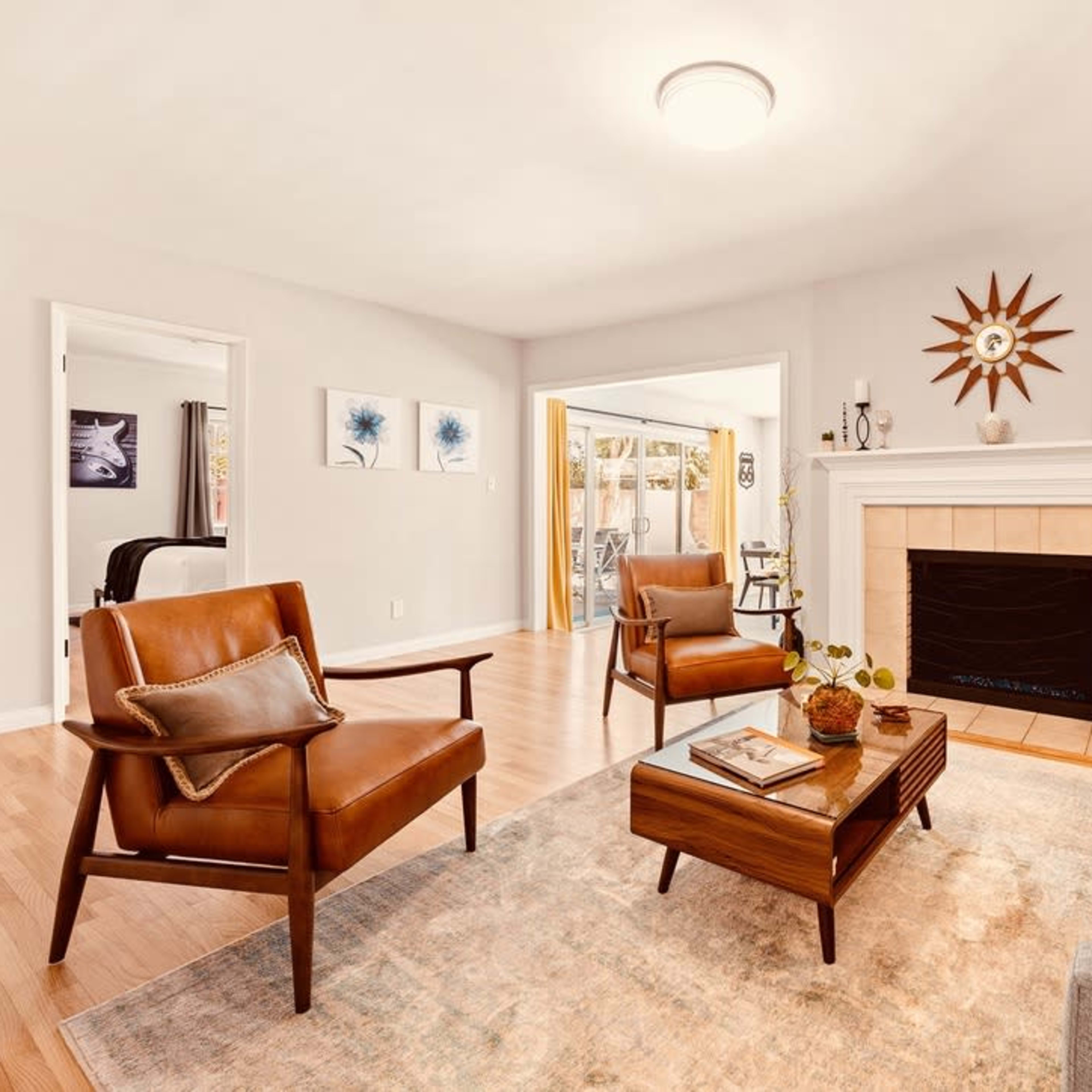 A modern living room features a gray sofa, brown leather chairs, a wooden coffee table, a stone fireplace, and a decorative sunburst wall clock.