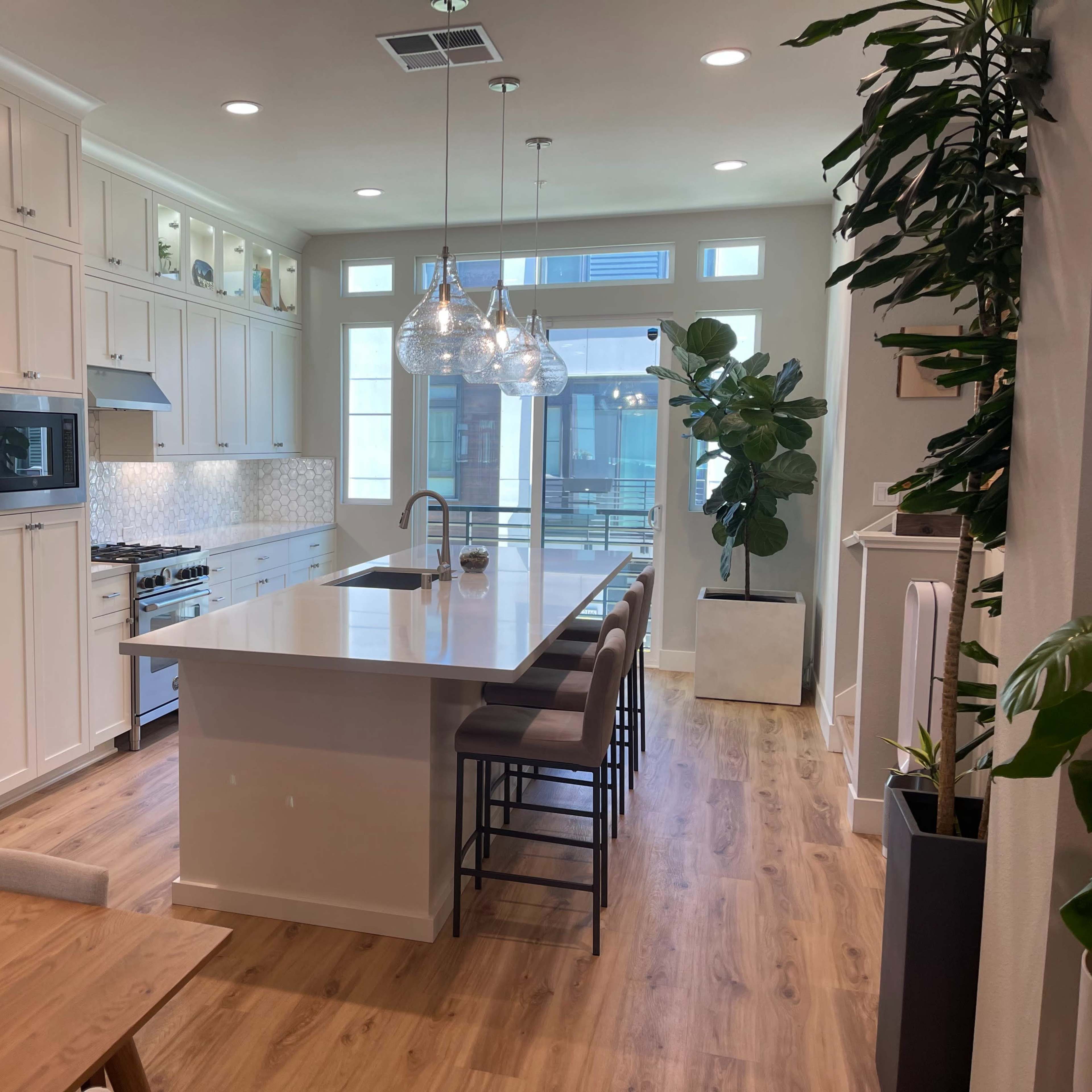 A modern kitchen with white cabinets, a large island with bar stools, and natural light streaming through large windows.