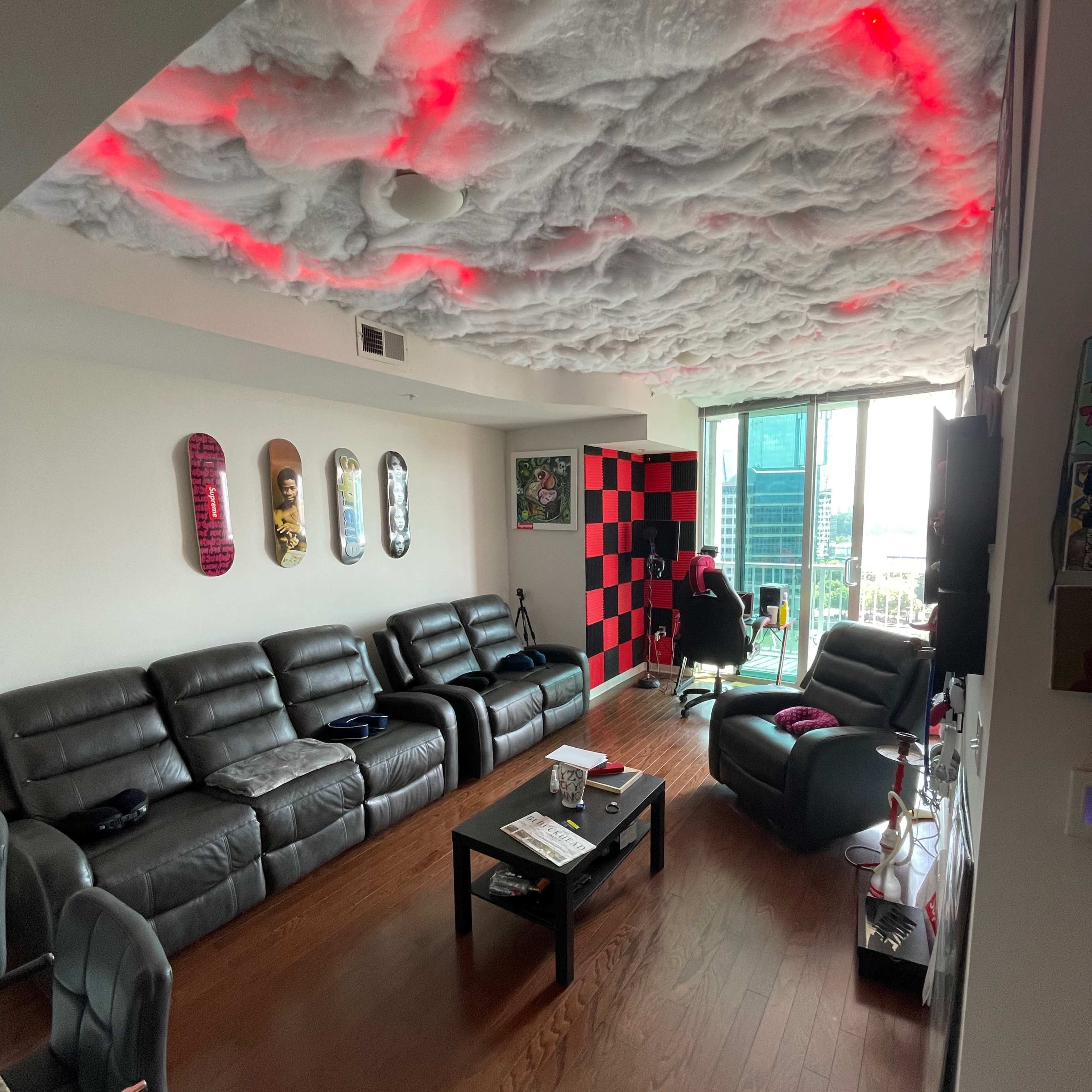 A living room features dark leather sofas, a checkered red and black wall, and a ceiling designed to resemble clouds with red lighting.