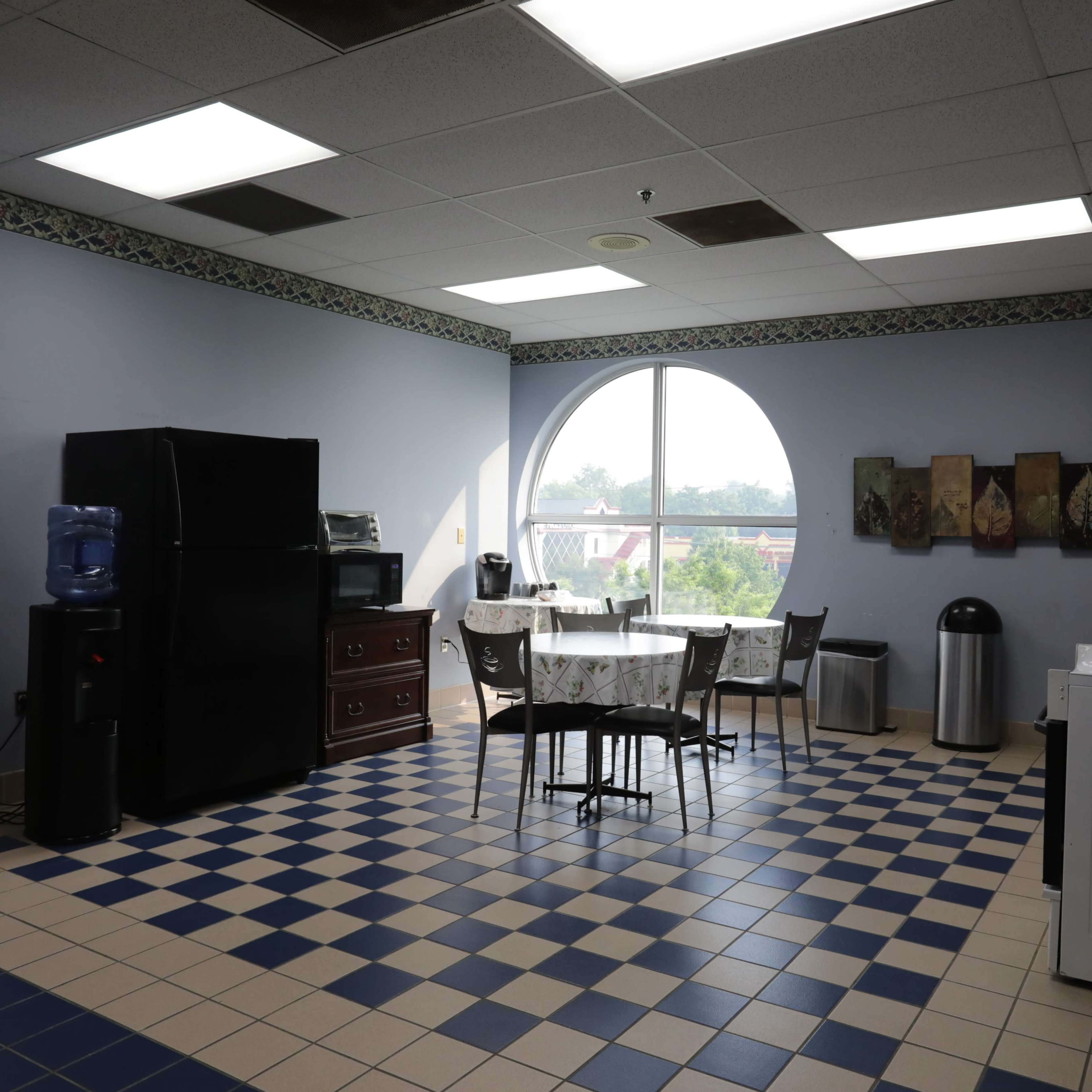 A kitchen area with a round window, a black refrigerator, a table with chairs, and a blue and white tiled floor.
