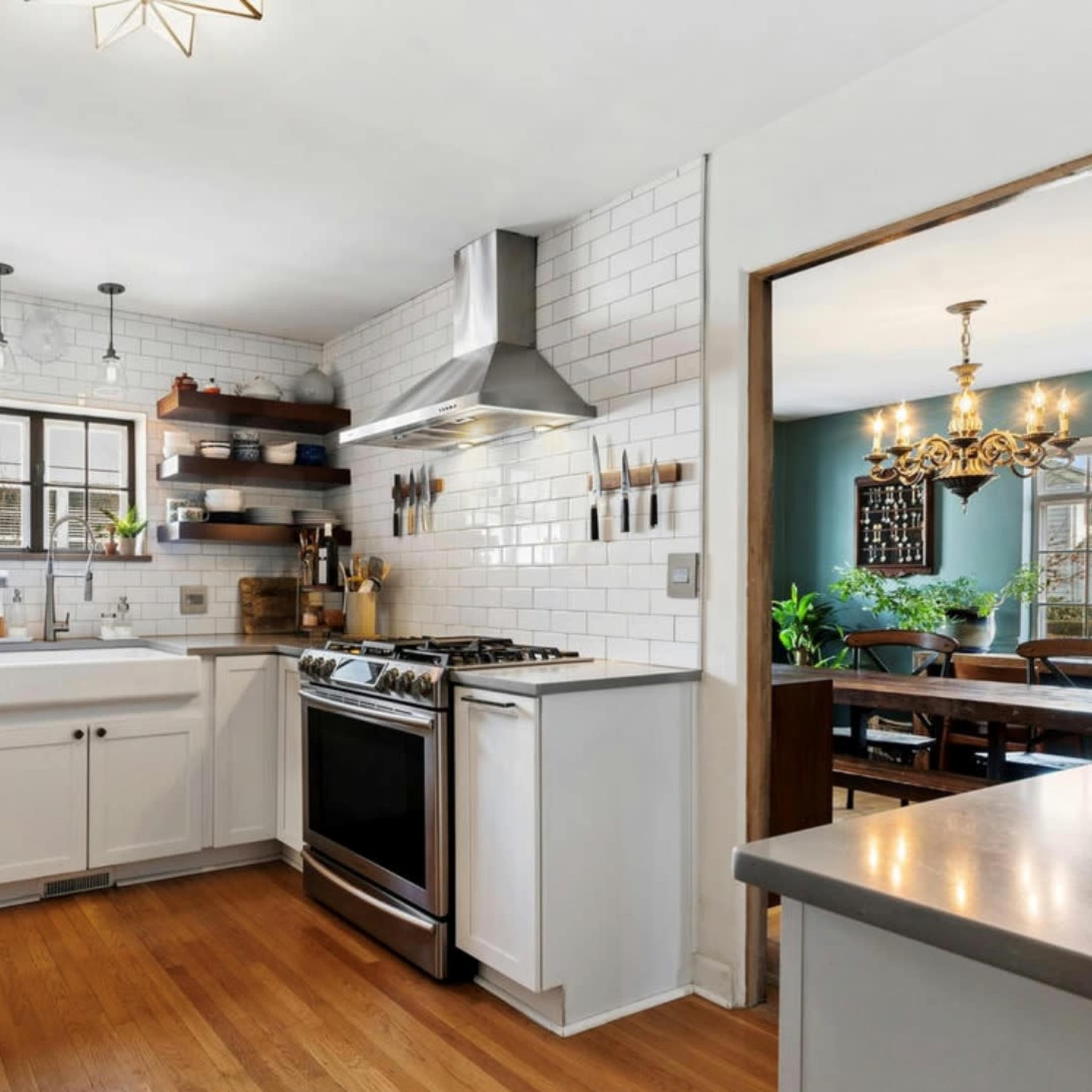 A modern kitchen features white cabinets, stainless steel appliances, and open shelving with various kitchen items against a tiled backsplash.