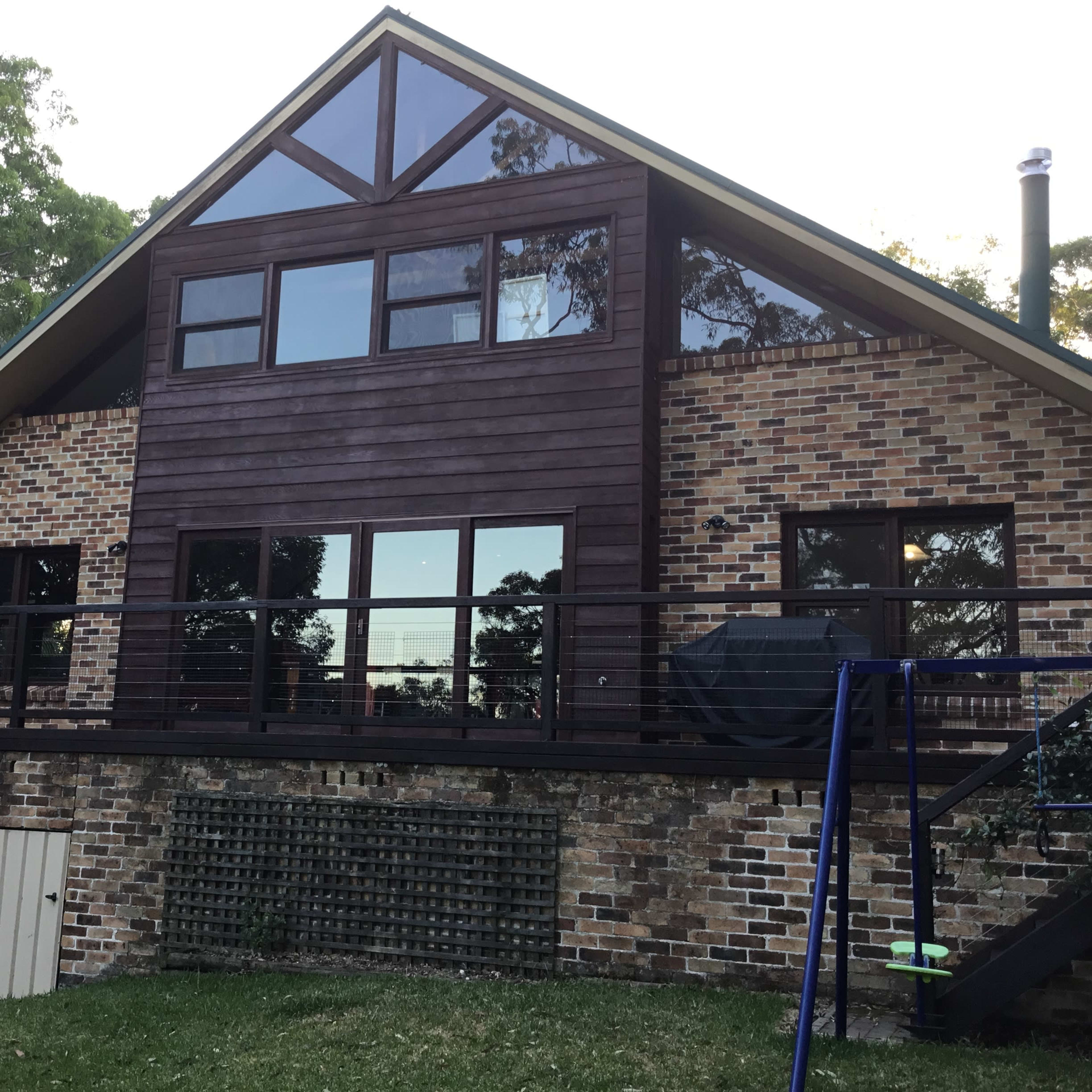 A two-story house with a combination of brick and wooden siding, featuring large windows and a balcony that overlooks a grassy yard.