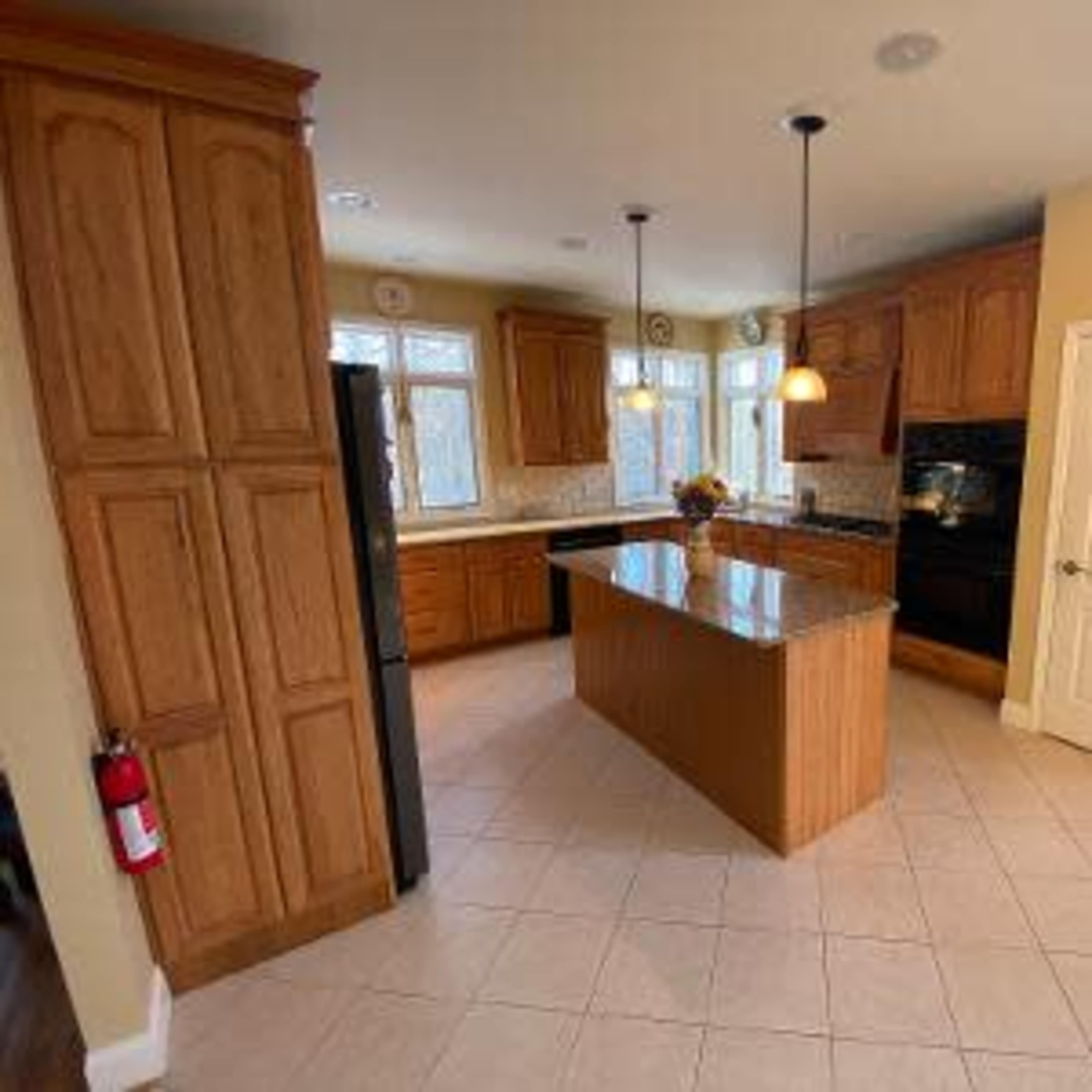 A spacious kitchen with wooden cabinets, a central island with a granite countertop, and tiled flooring.