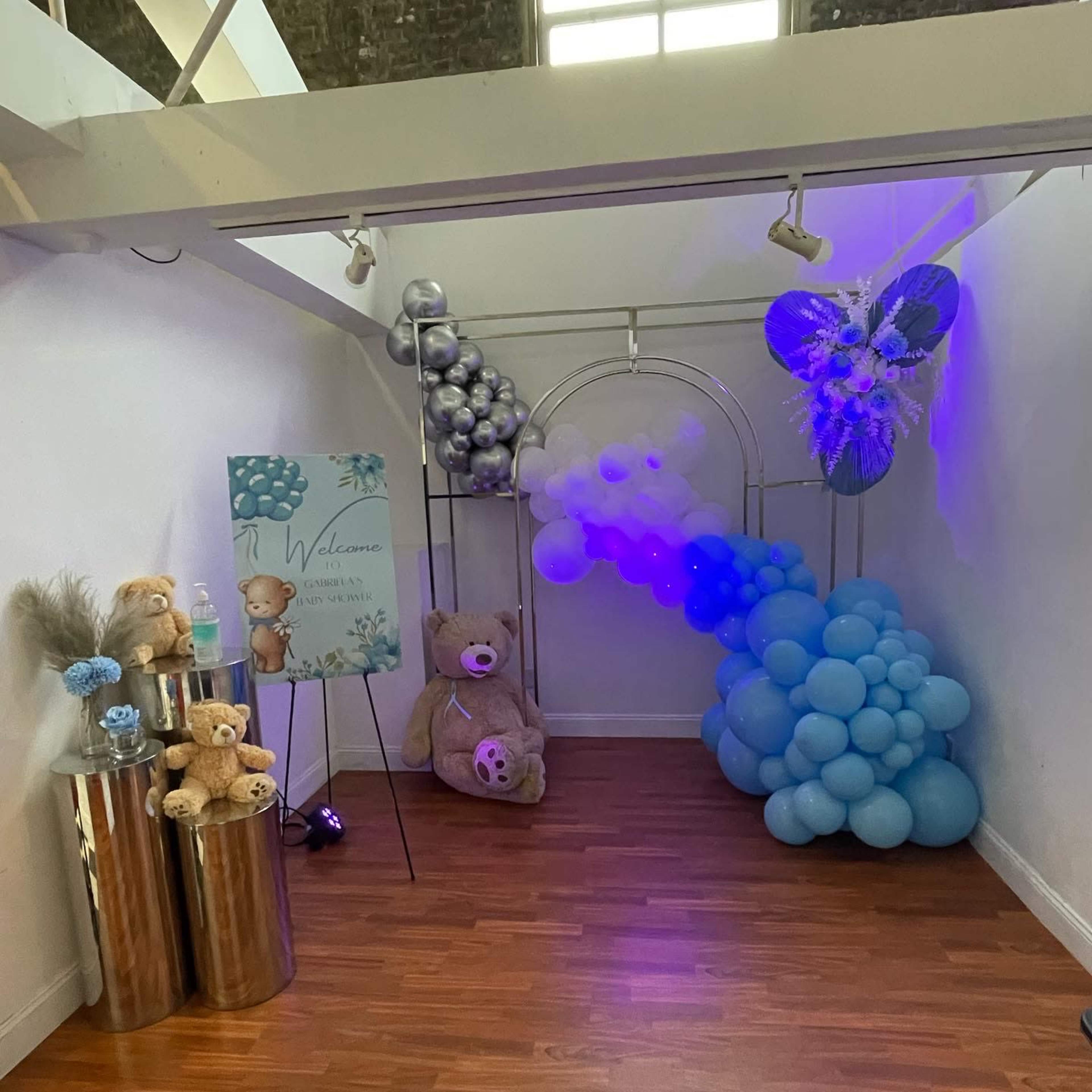 A decorated corner of a room featuring a balloon arch in shades of blue, stuffed bears, and a welcome sign.
