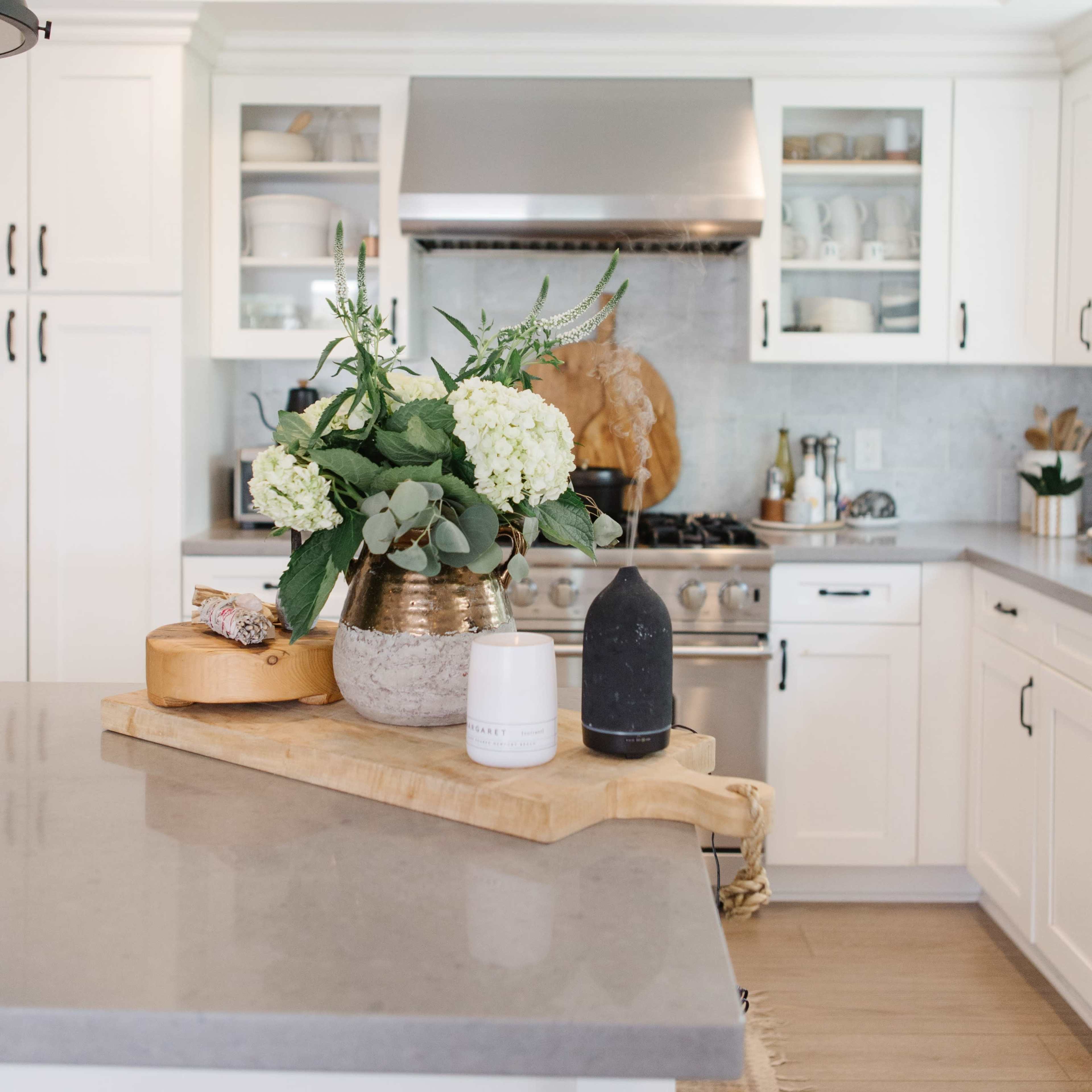 A modern kitchen features a stove, white cabinetry, and a countertop with a floral arrangement and wooden cutting board.