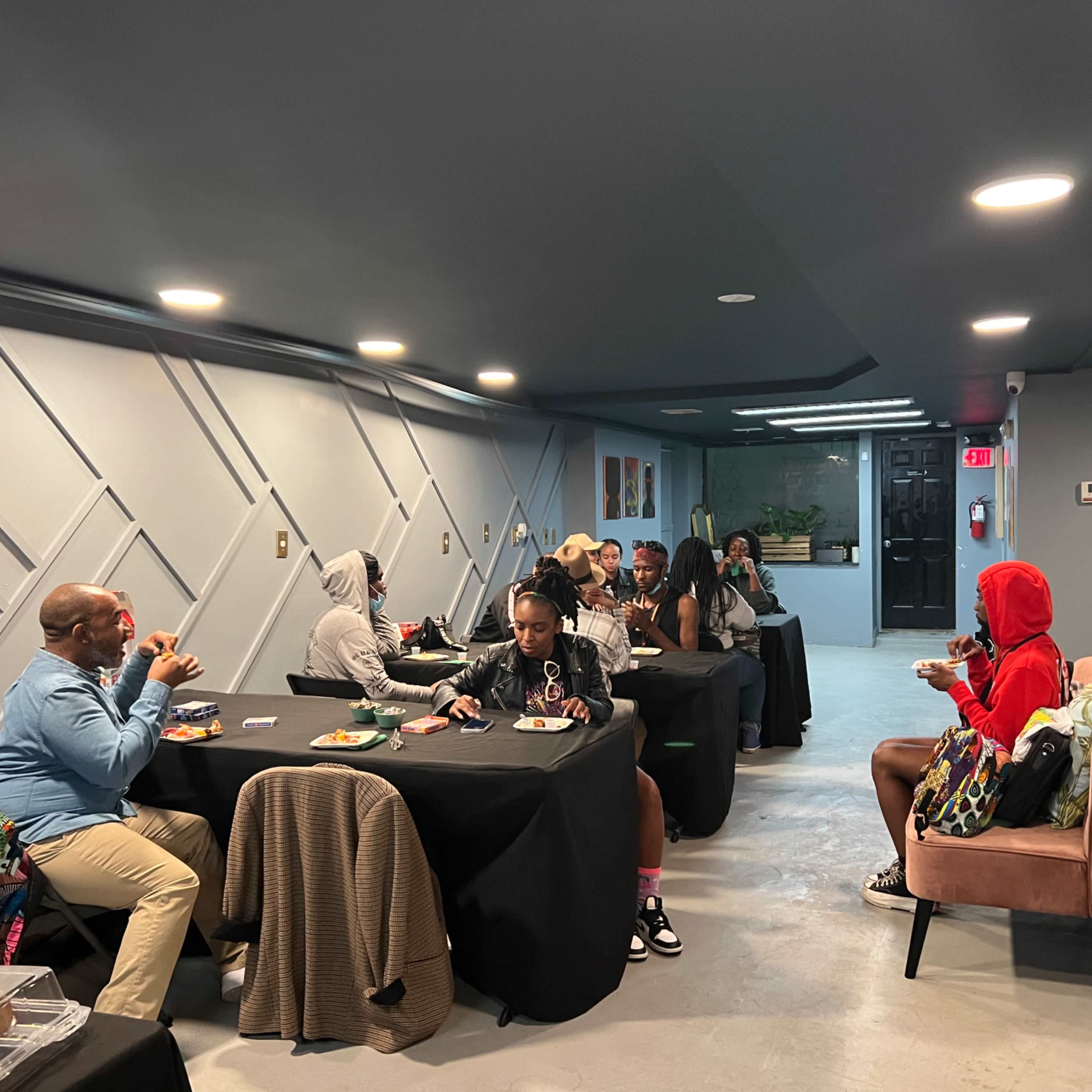 A group of people is seated at tables in a dimly lit room, enjoying food and engaging in conversation.