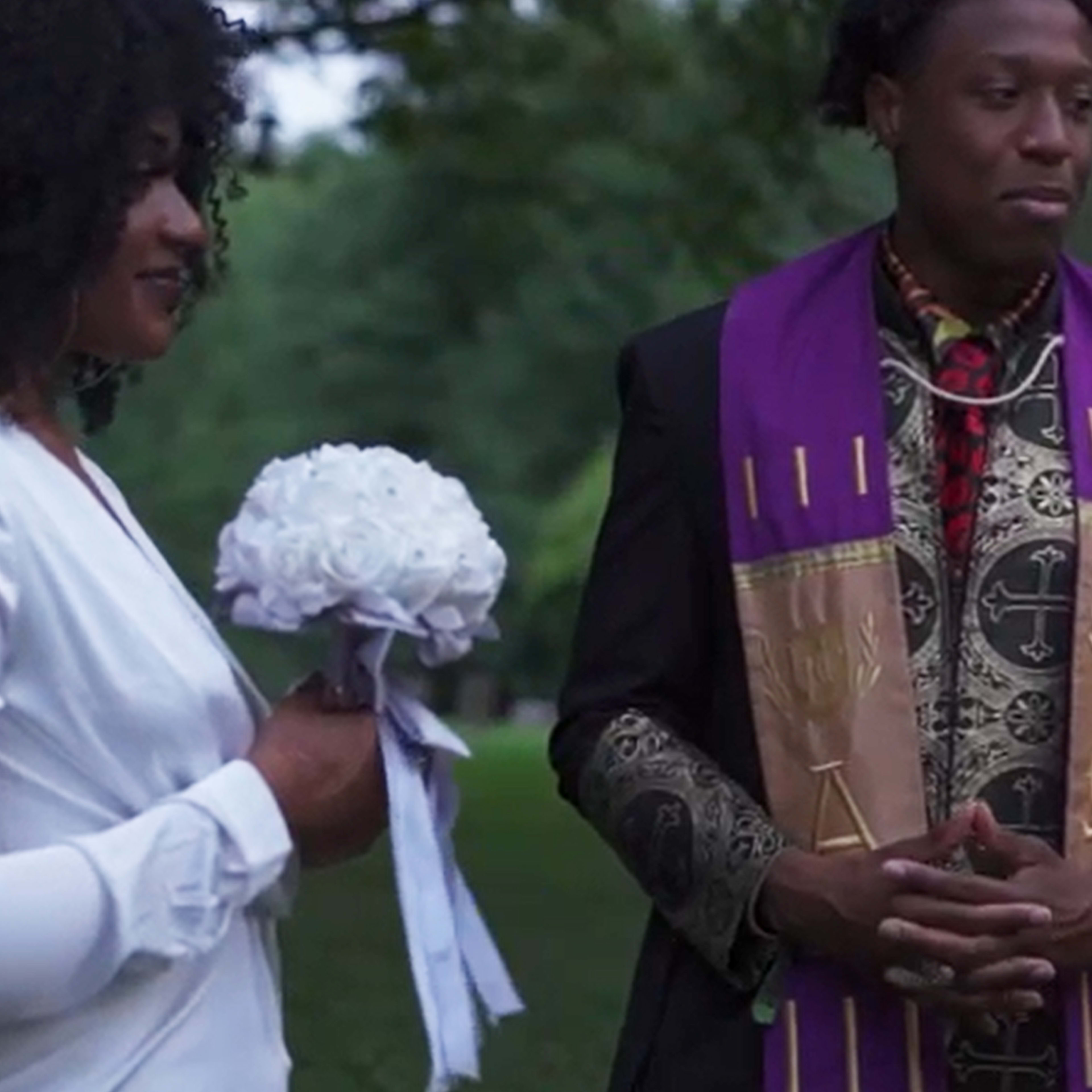 A woman in a white dress holds a bouquet while standing next to a man in traditional ceremonial attire.