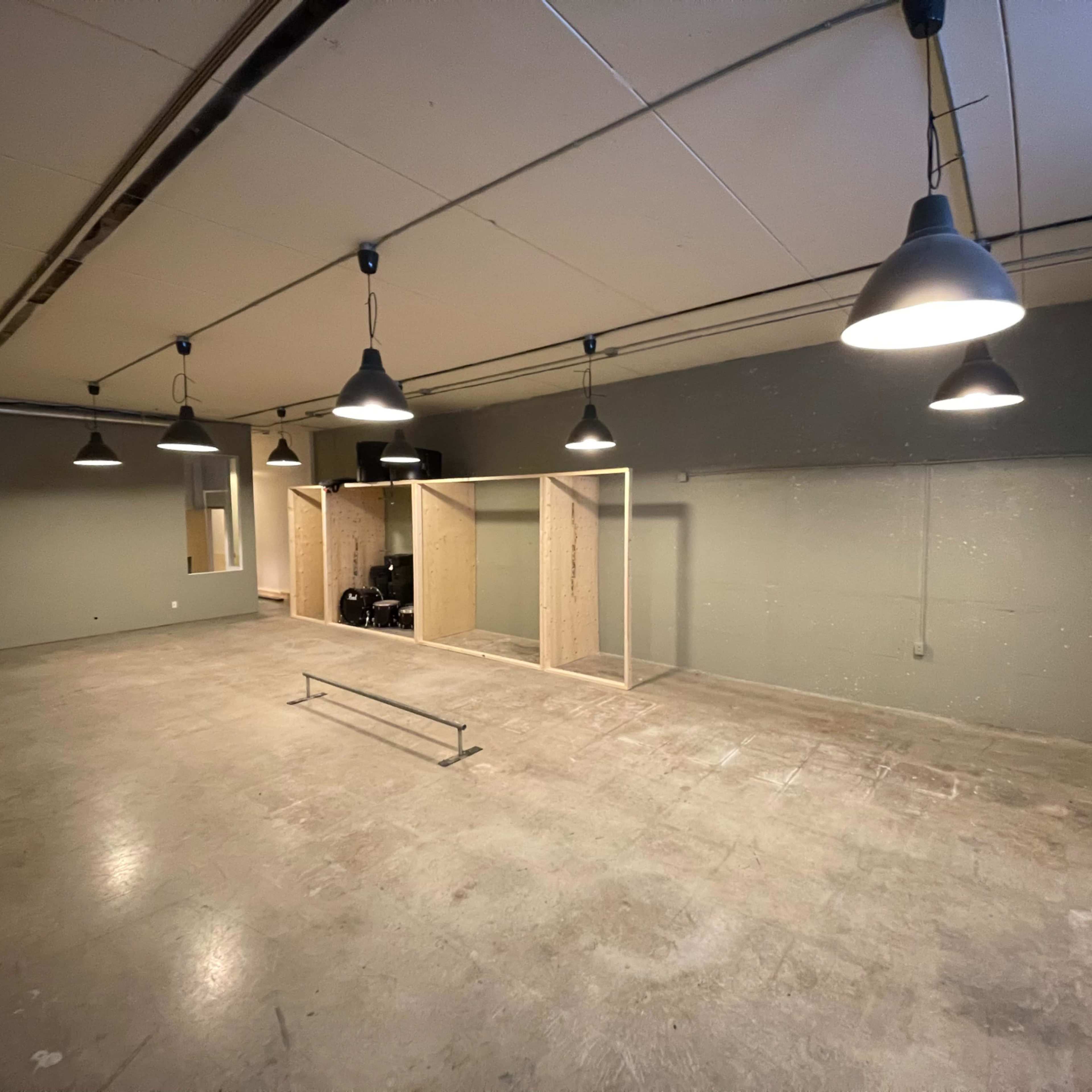 A spacious, industrial-style room with concrete flooring, exposed lighting fixtures, and a partitioned area on one side.
