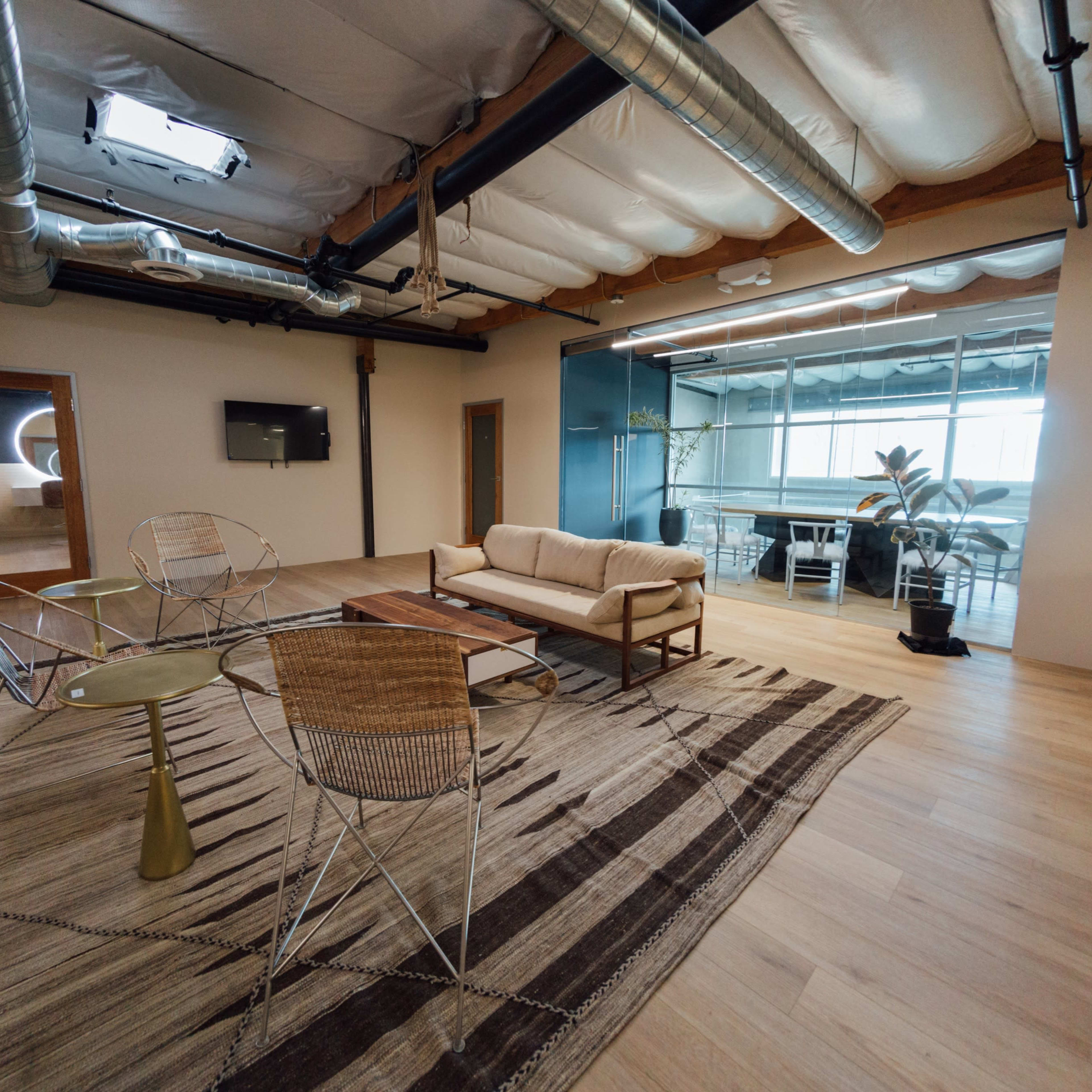 A modern office interior featuring a seating area with a couch and chairs, a coffee table, and glass-walled meeting rooms in the background.