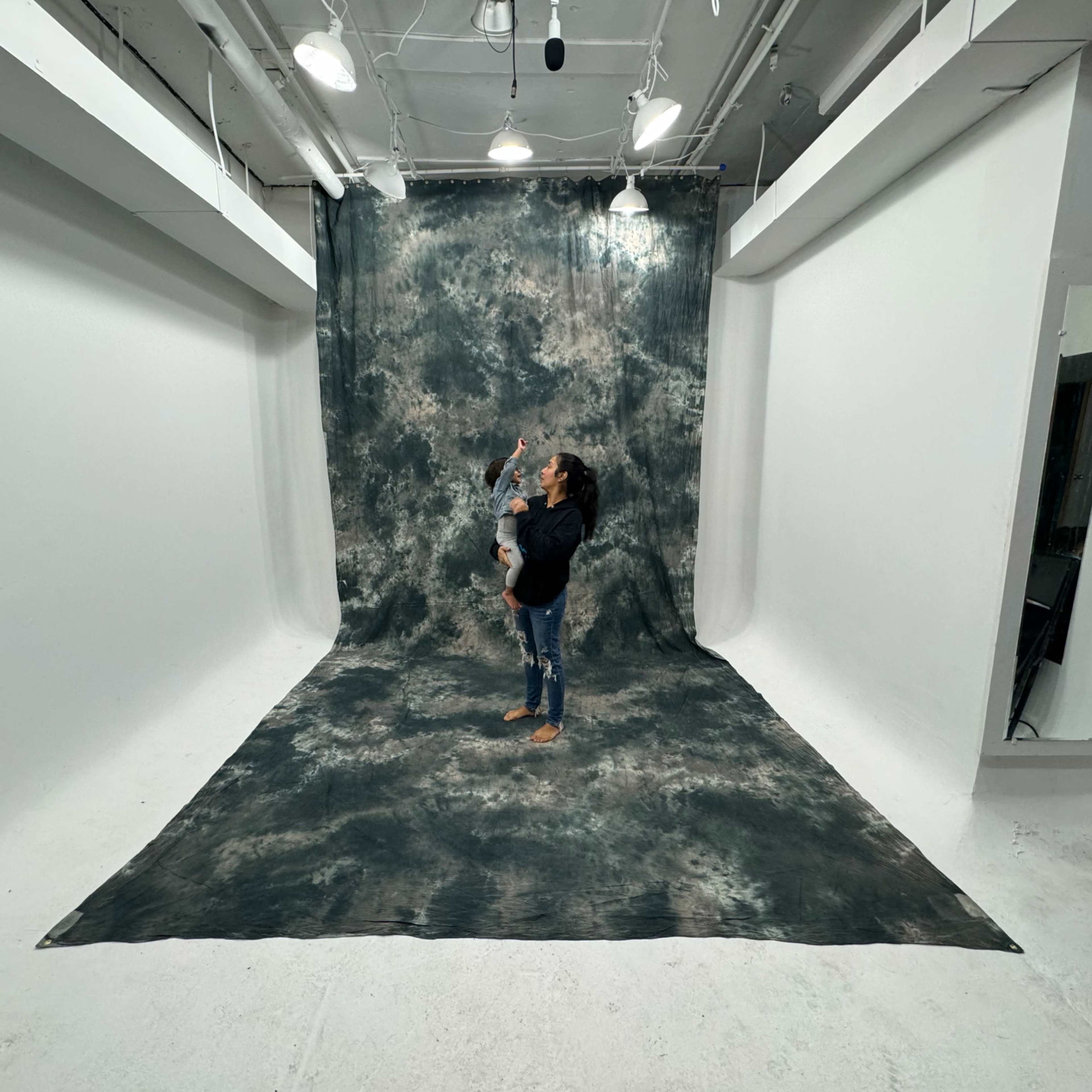 An empty, white photography studio with overhead lighting and a mirror on the wall.