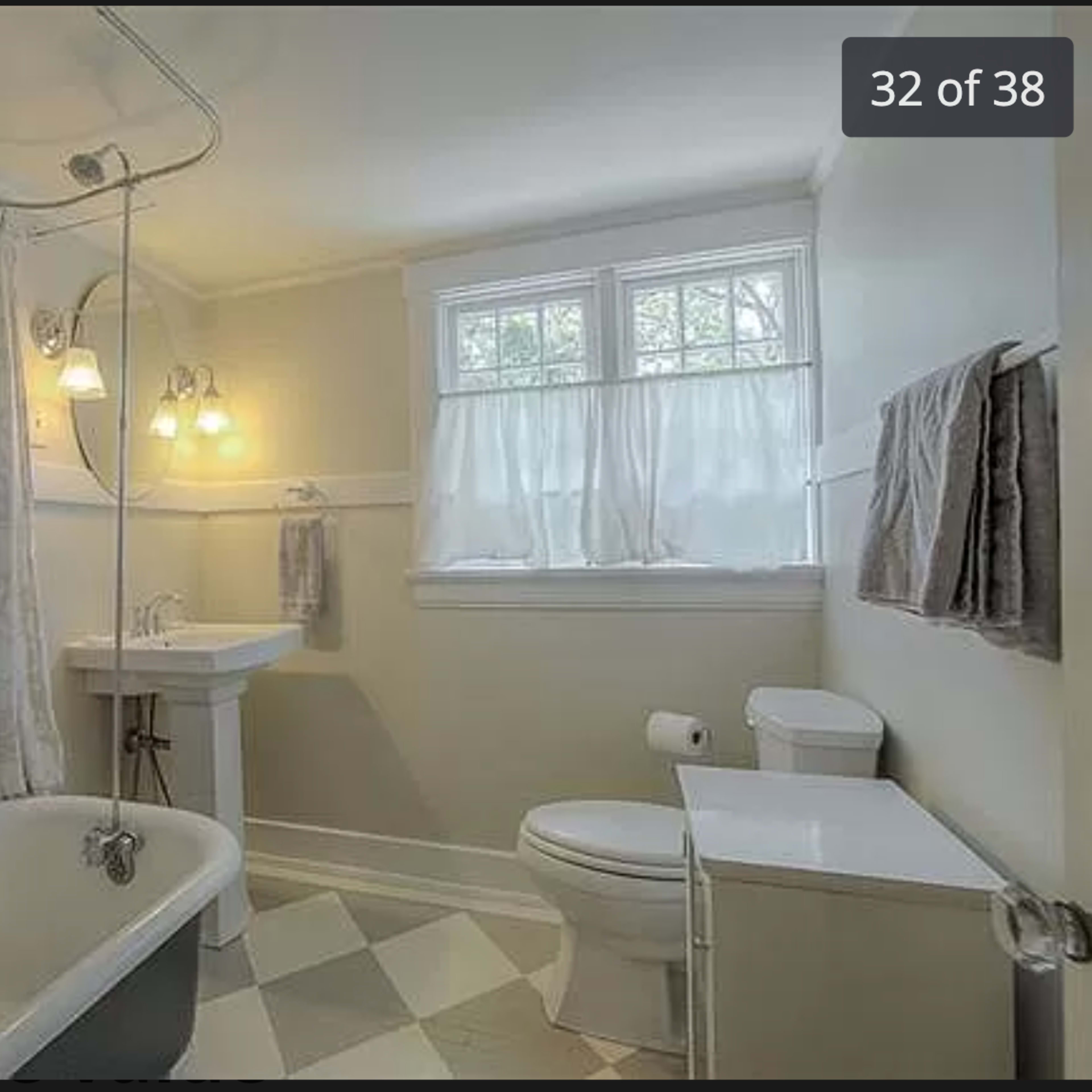 A bathroom featuring a clawfoot tub, a pedestal sink, a toilet, and a window with sheer curtains.