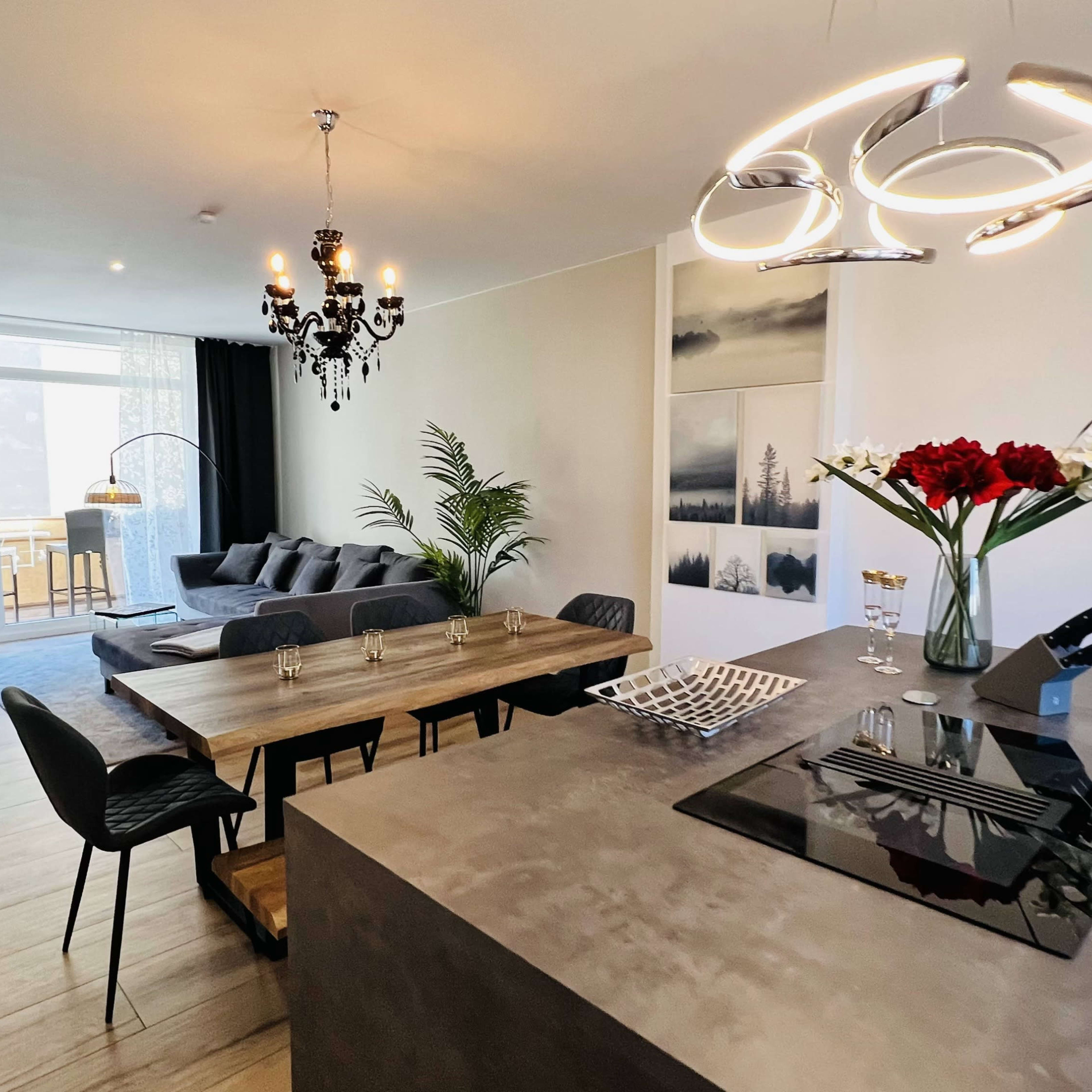 A modern open-concept living and dining area features a sleek kitchen island, a wooden dining table with black chairs, and a cozy seating area with a large sofa.