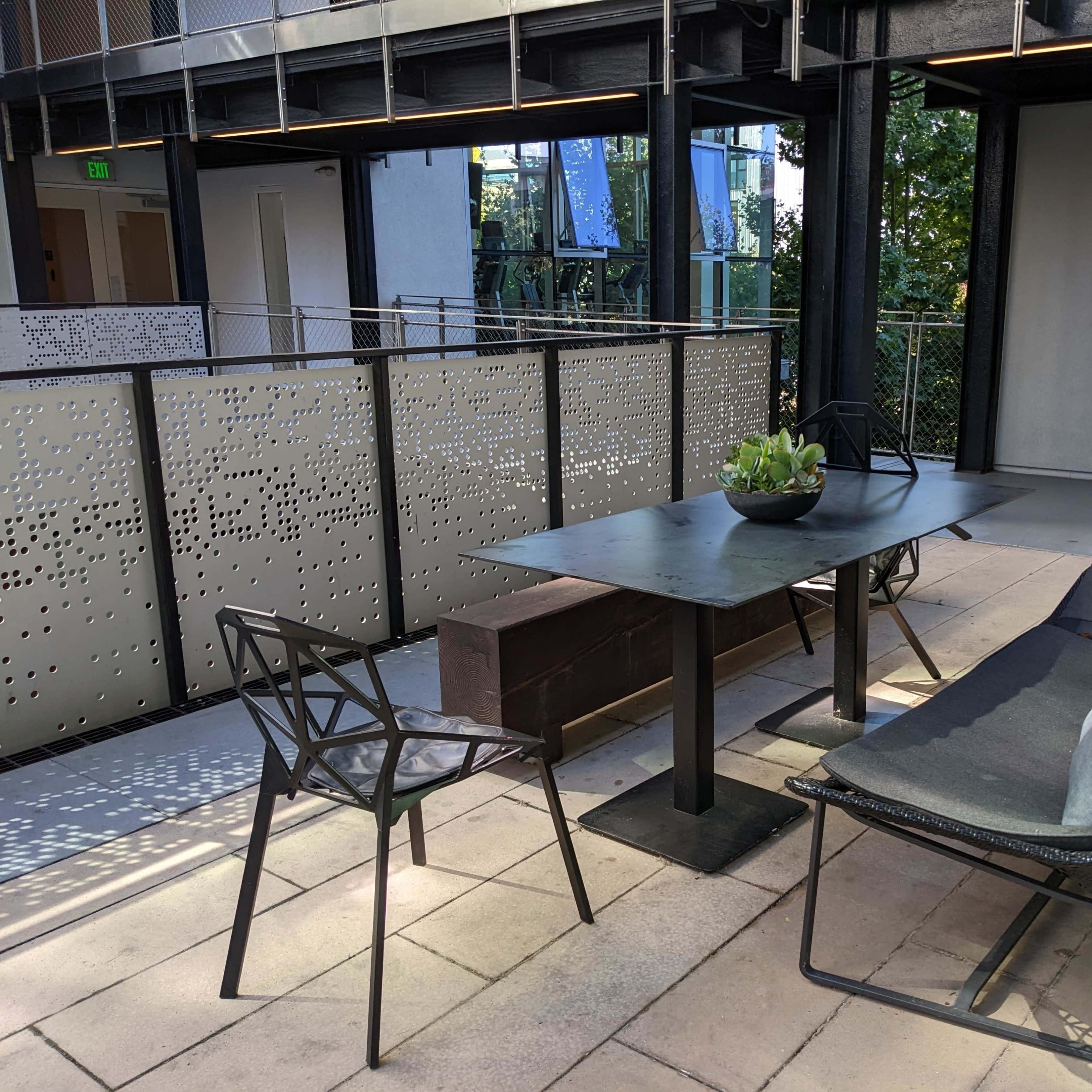 A modern outdoor space features a table with a plant centerpiece and seating options on a paved surface.