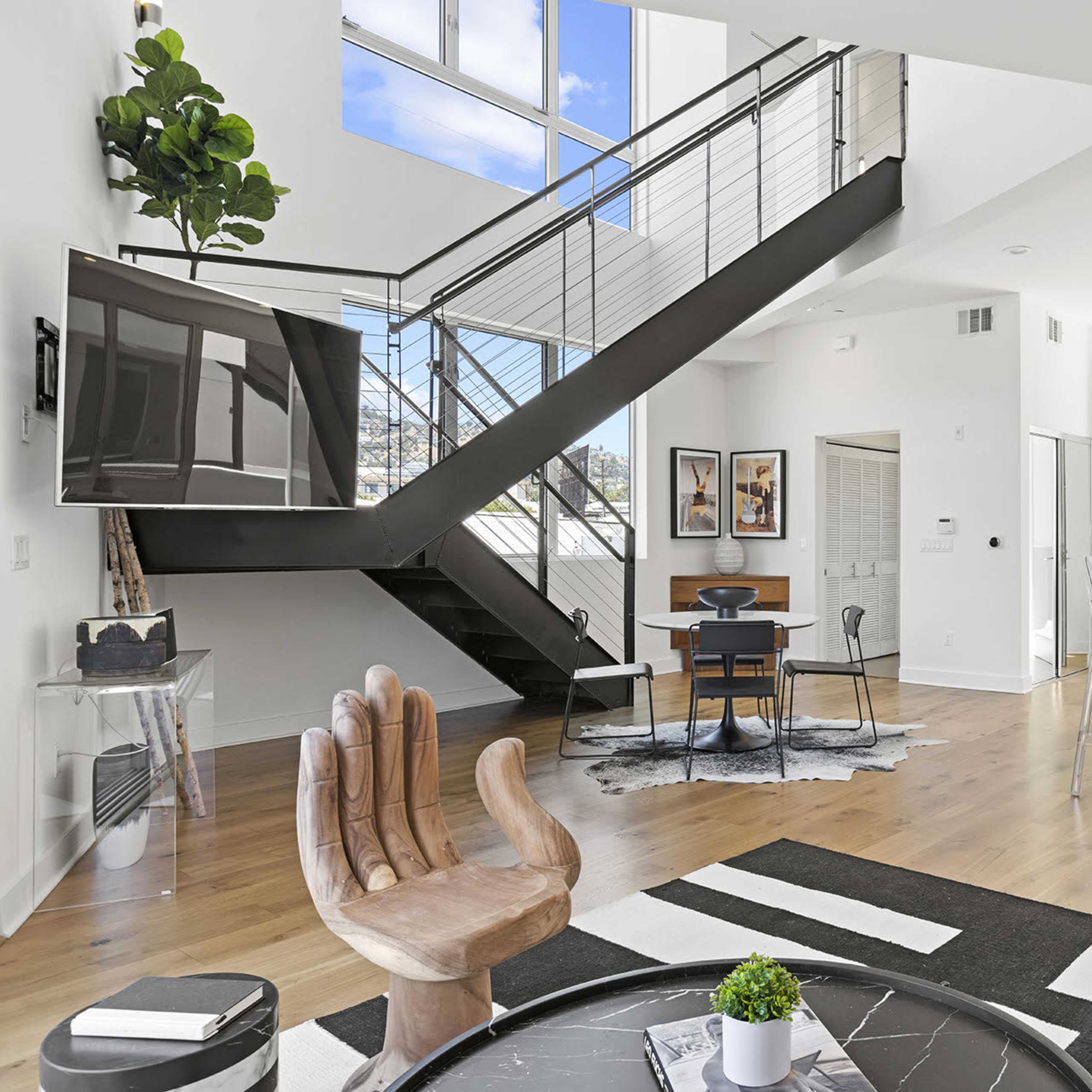 A modern, open-concept living space with a sleek staircase, a dining area, and a kitchen featuring minimalist designs and large windows.
