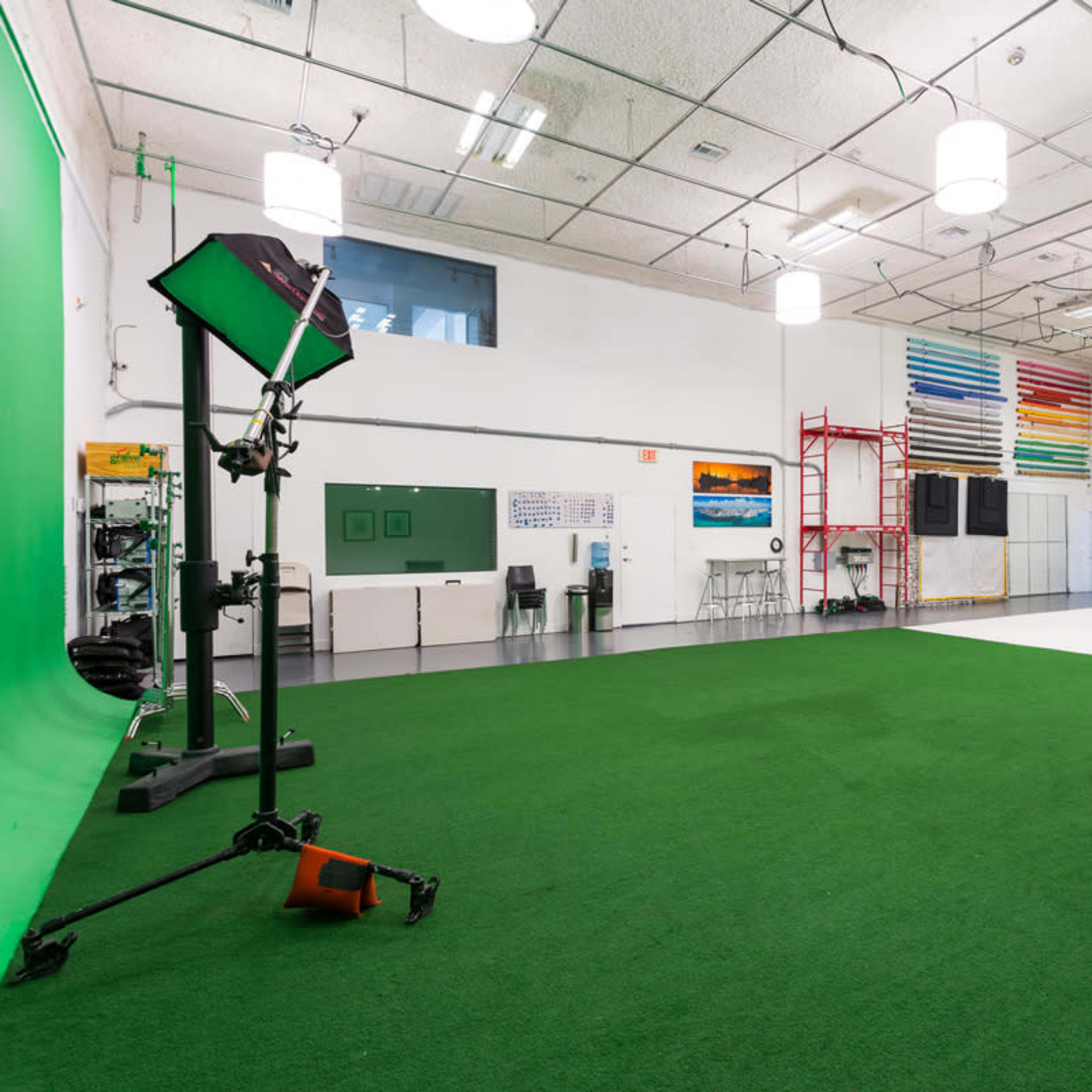 A spacious studio with a green screen, various lighting equipment, and a white backdrop, all set against a carpet of artificial grass.