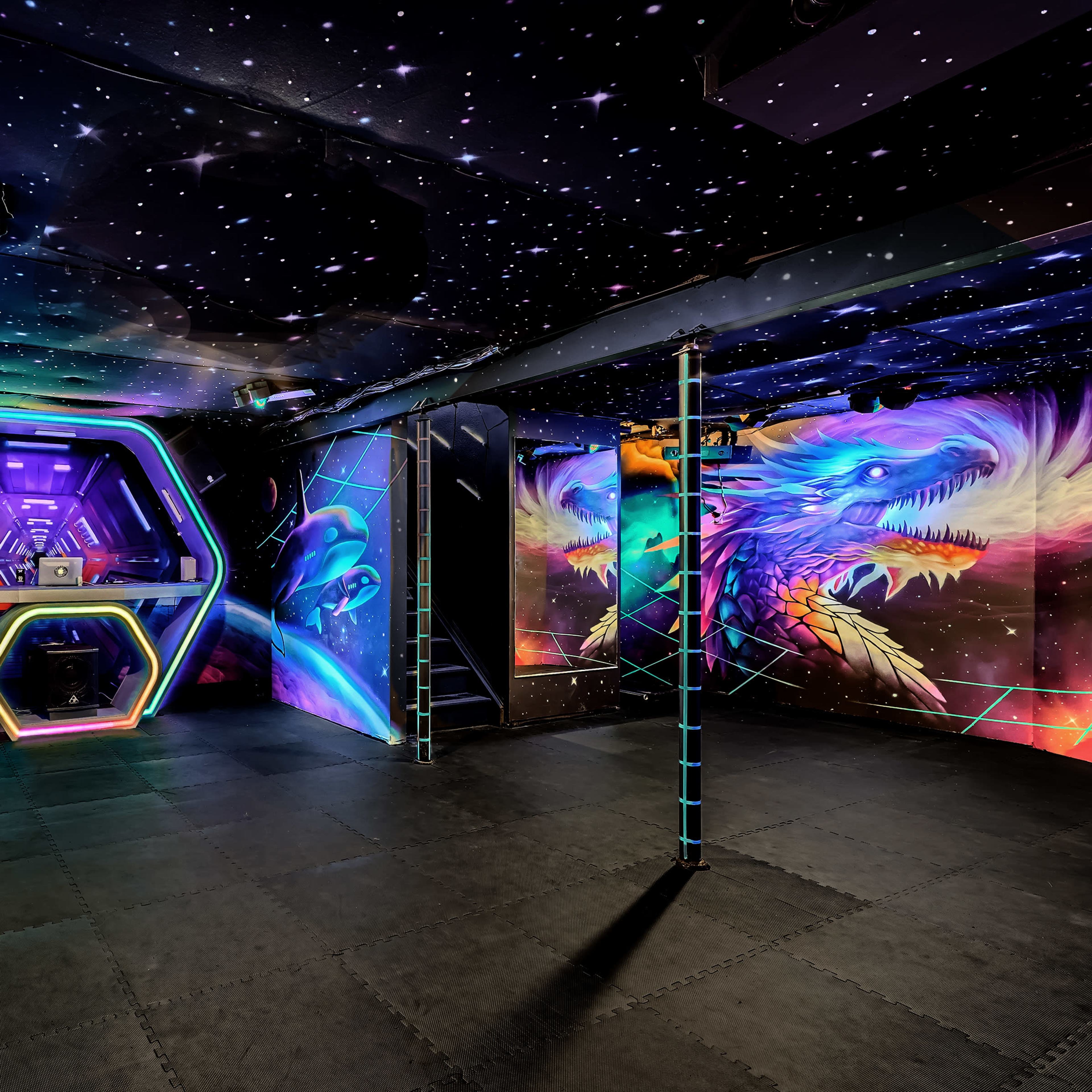 A dark, illuminated room with vibrant neon murals of animals and a central DJ booth surrounded by colorful, starry wall art.