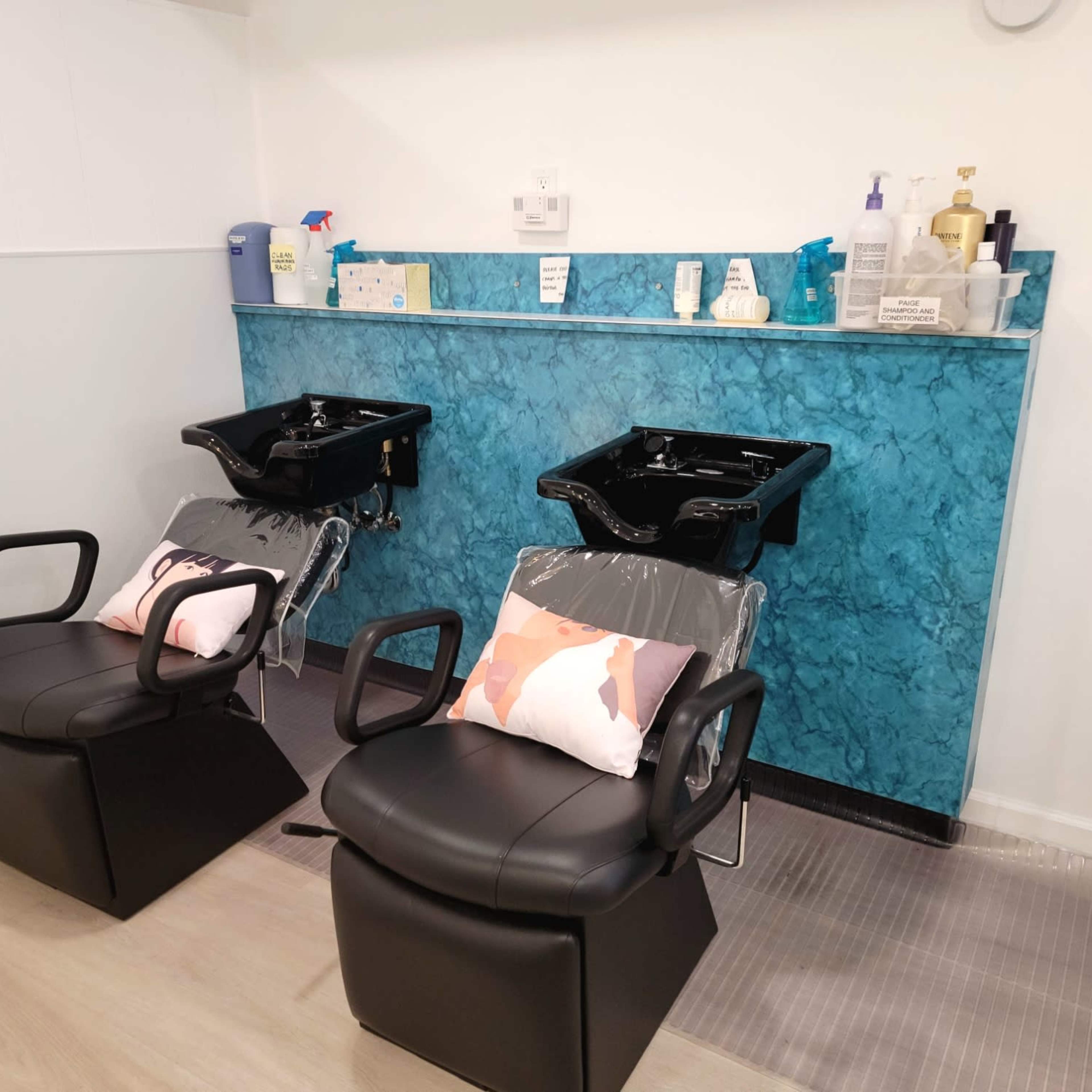 Two black salon chairs with sink basins set against a blue marble wall in a hair salon.