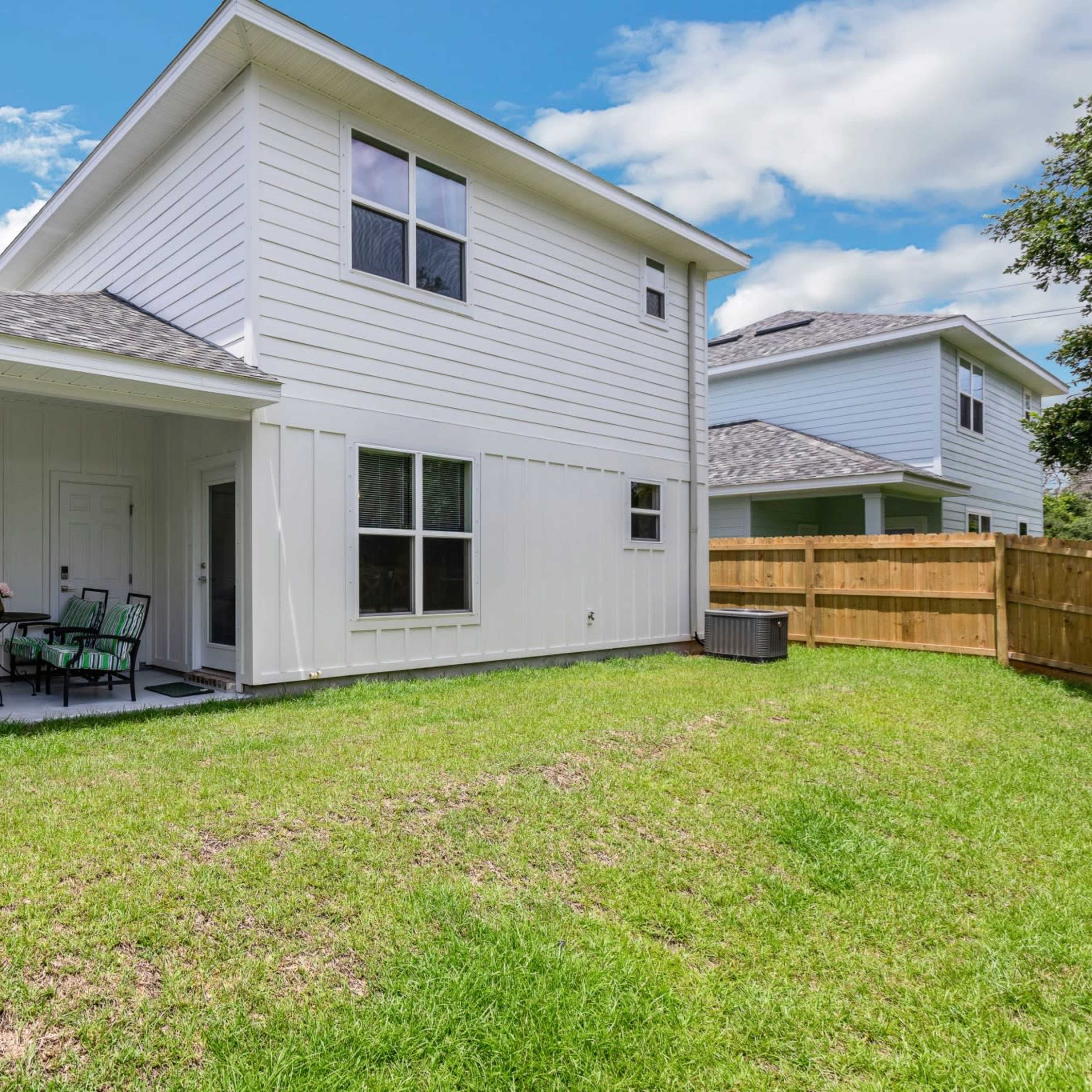 A two-story white house with a fenced backyard featuring a patio set on a grassy area.