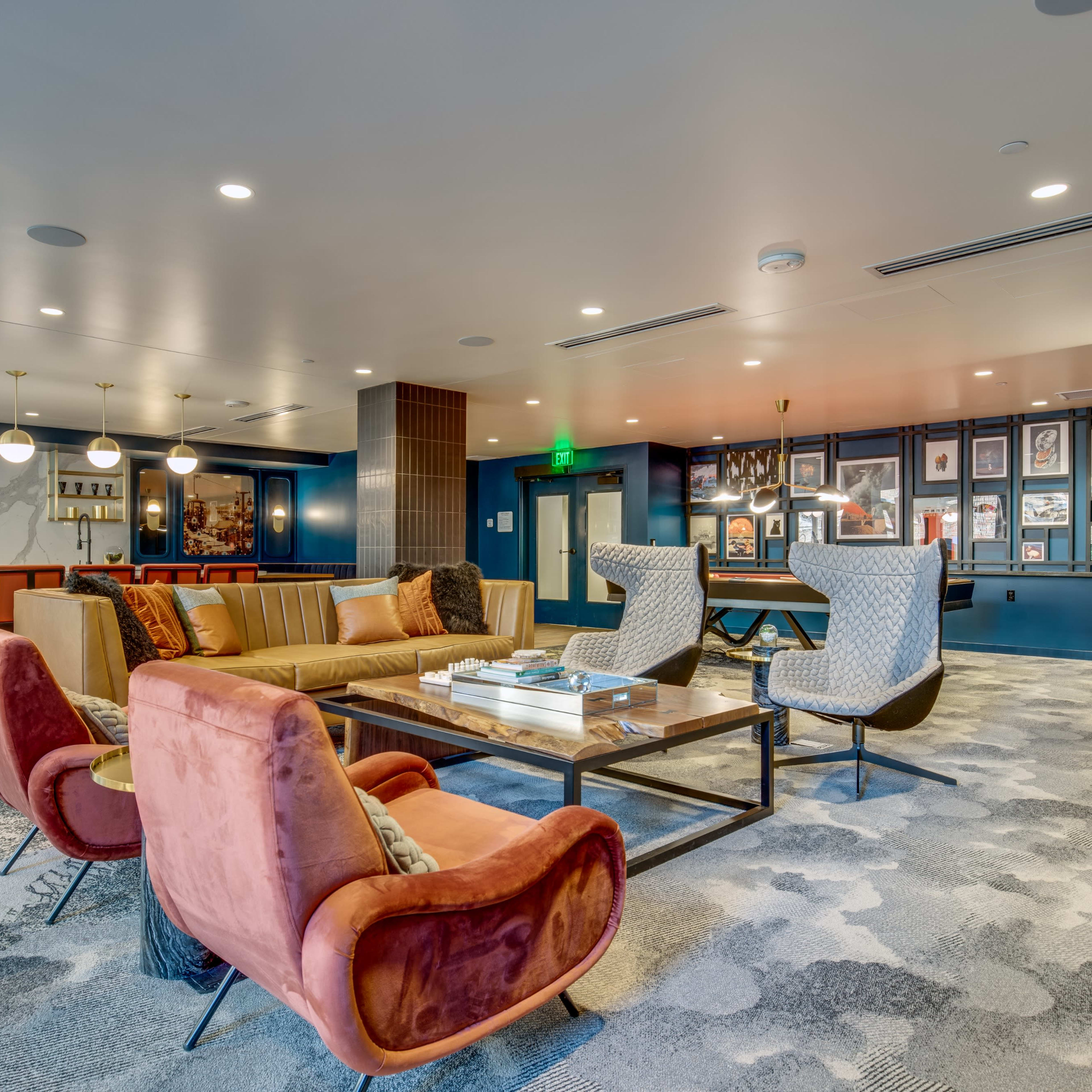 A modern lounge area featuring a seating arrangement with colorful armchairs and a sofa, a coffee table, and framed artwork on the walls.