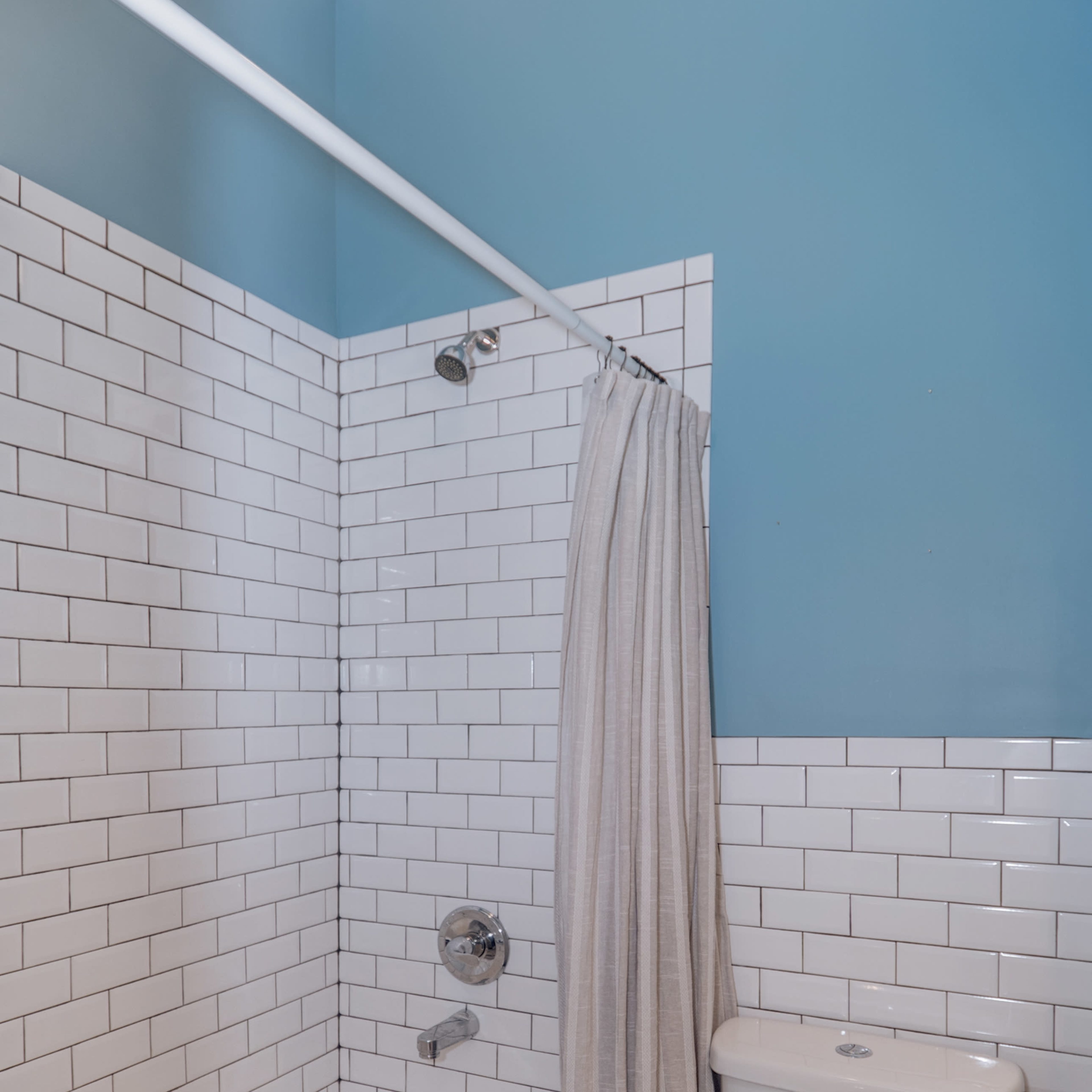 A small bathroom with a bathtub and shower, a toilet, and white tiled walls with a blue-painted upper section.