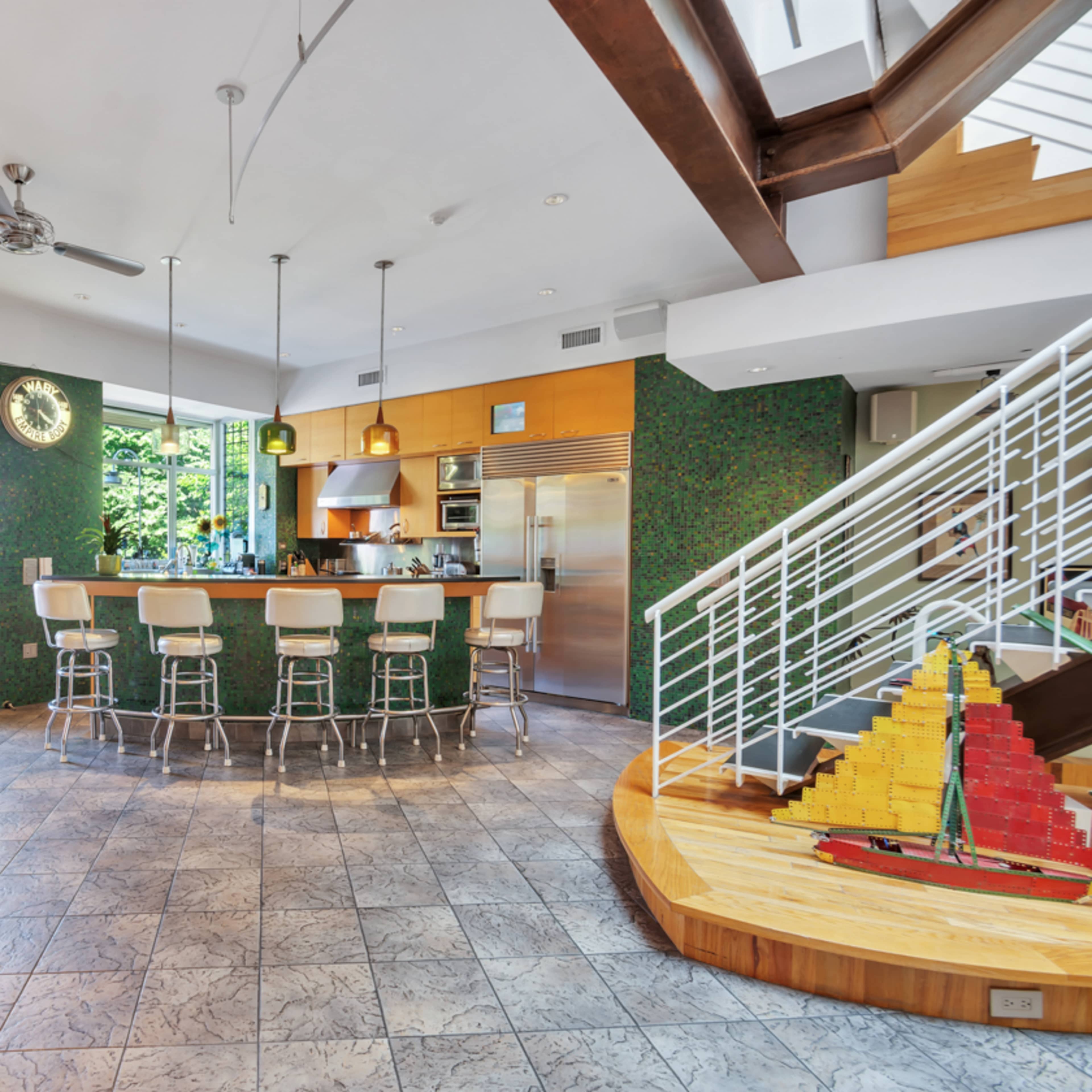 A modern kitchen with a central bar area, surrounded by green wallpaper and featuring a staircase leading to an upper level.