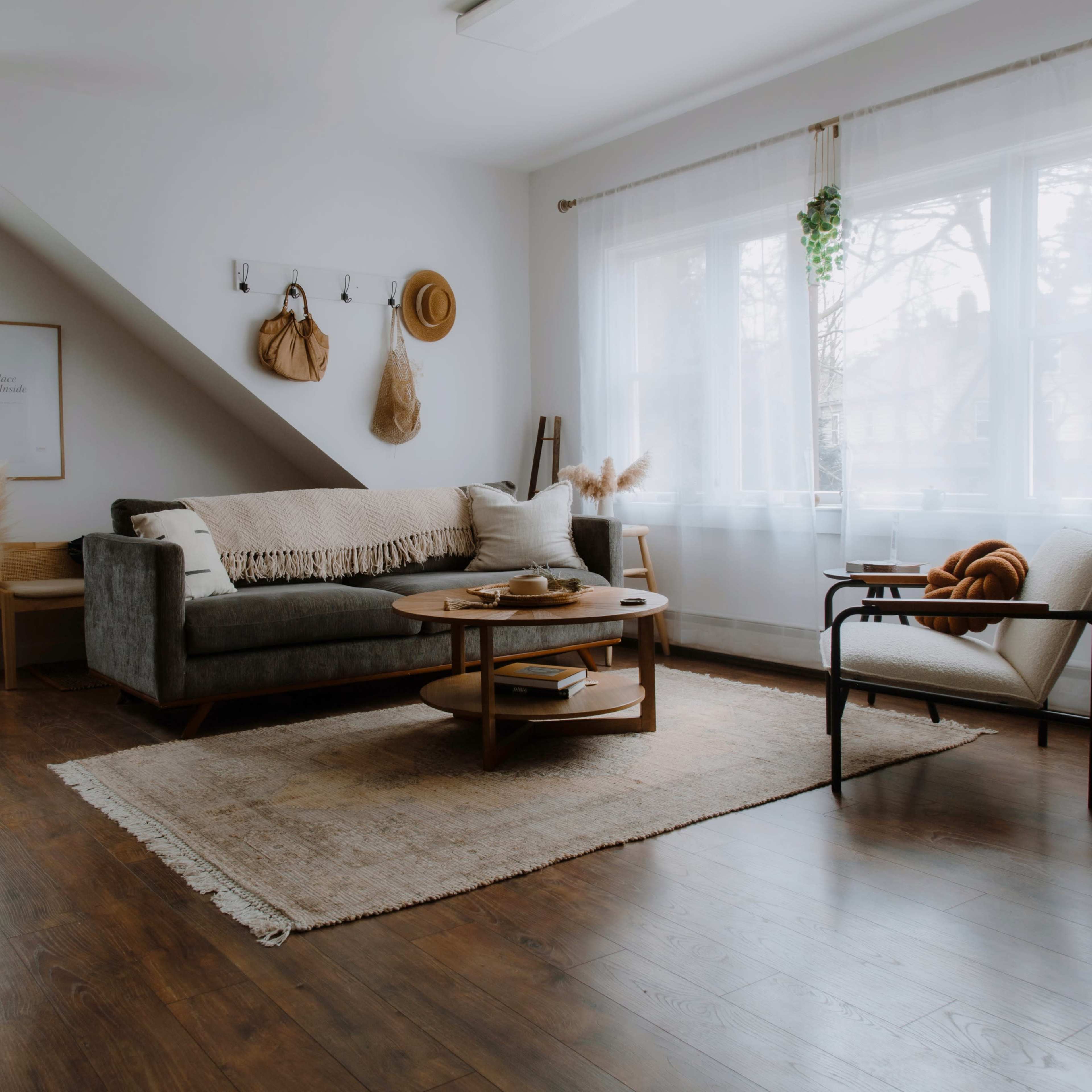 A minimalist living room features a gray sofa, a round coffee table, and a large window with sheer curtains, all set against wooden flooring.