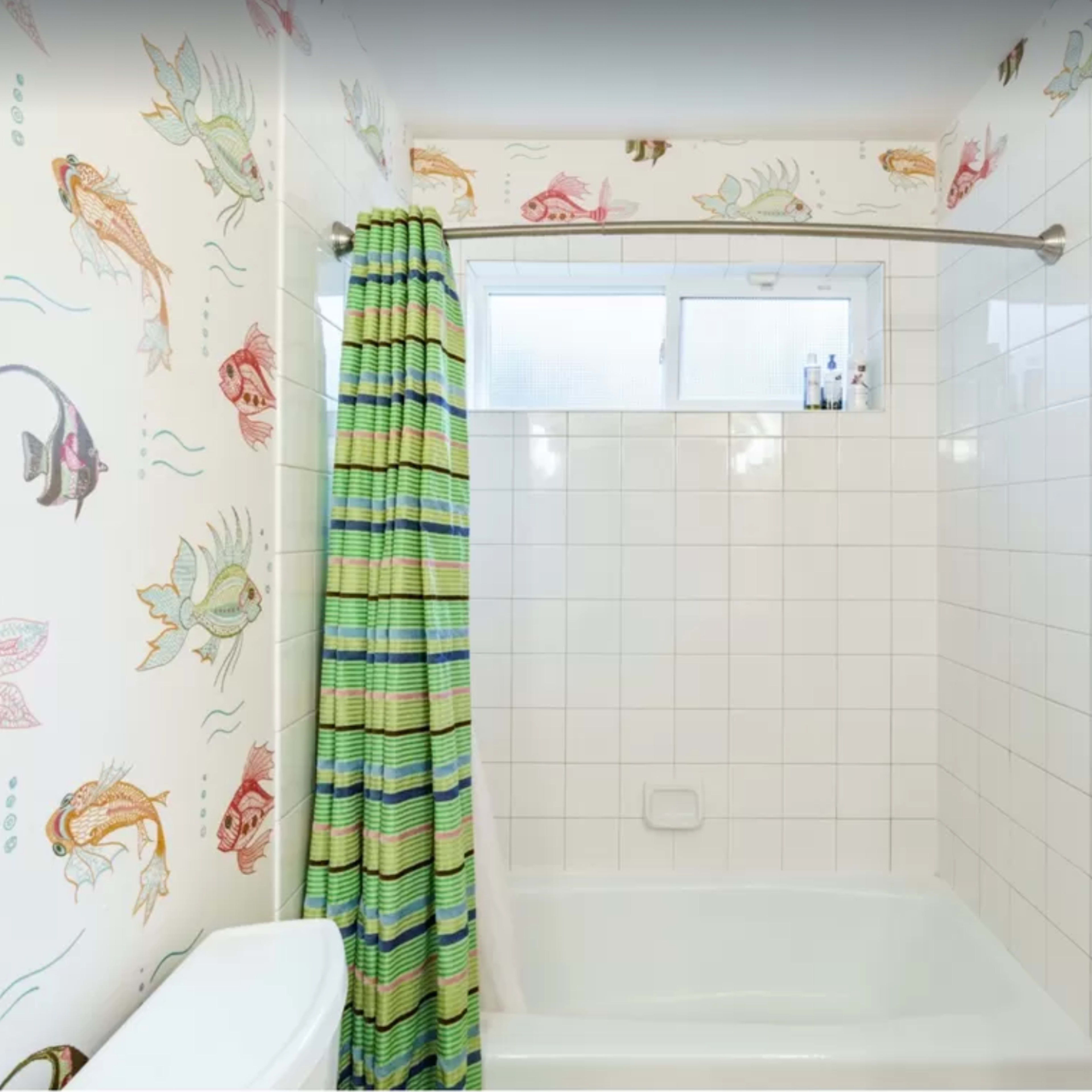 A bathroom with a bathtub, tiled walls featuring fish decorations, and a green and blue striped shower curtain.