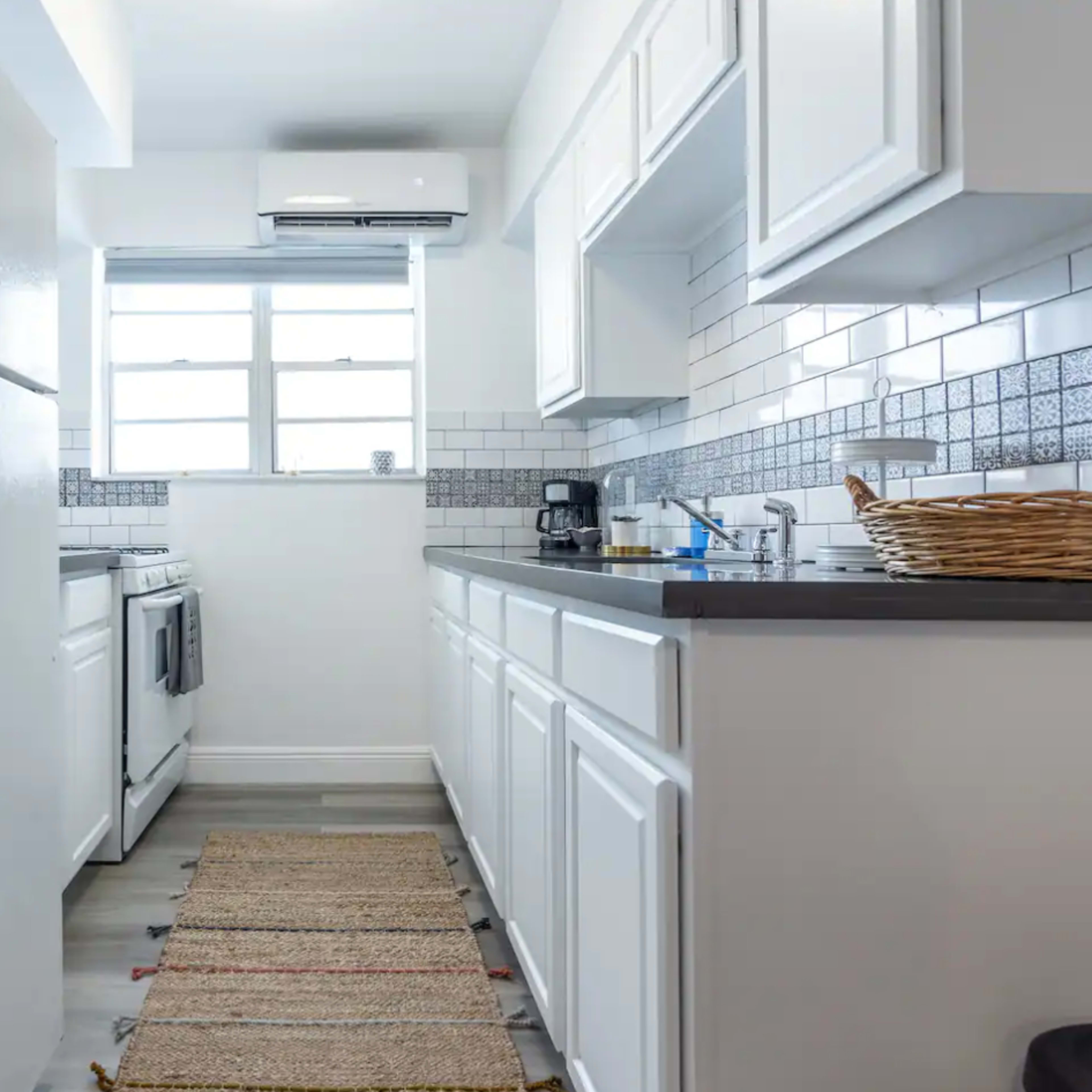 A narrow kitchen features white cabinetry, stainless steel appliances, and a patterned rug along the floor.