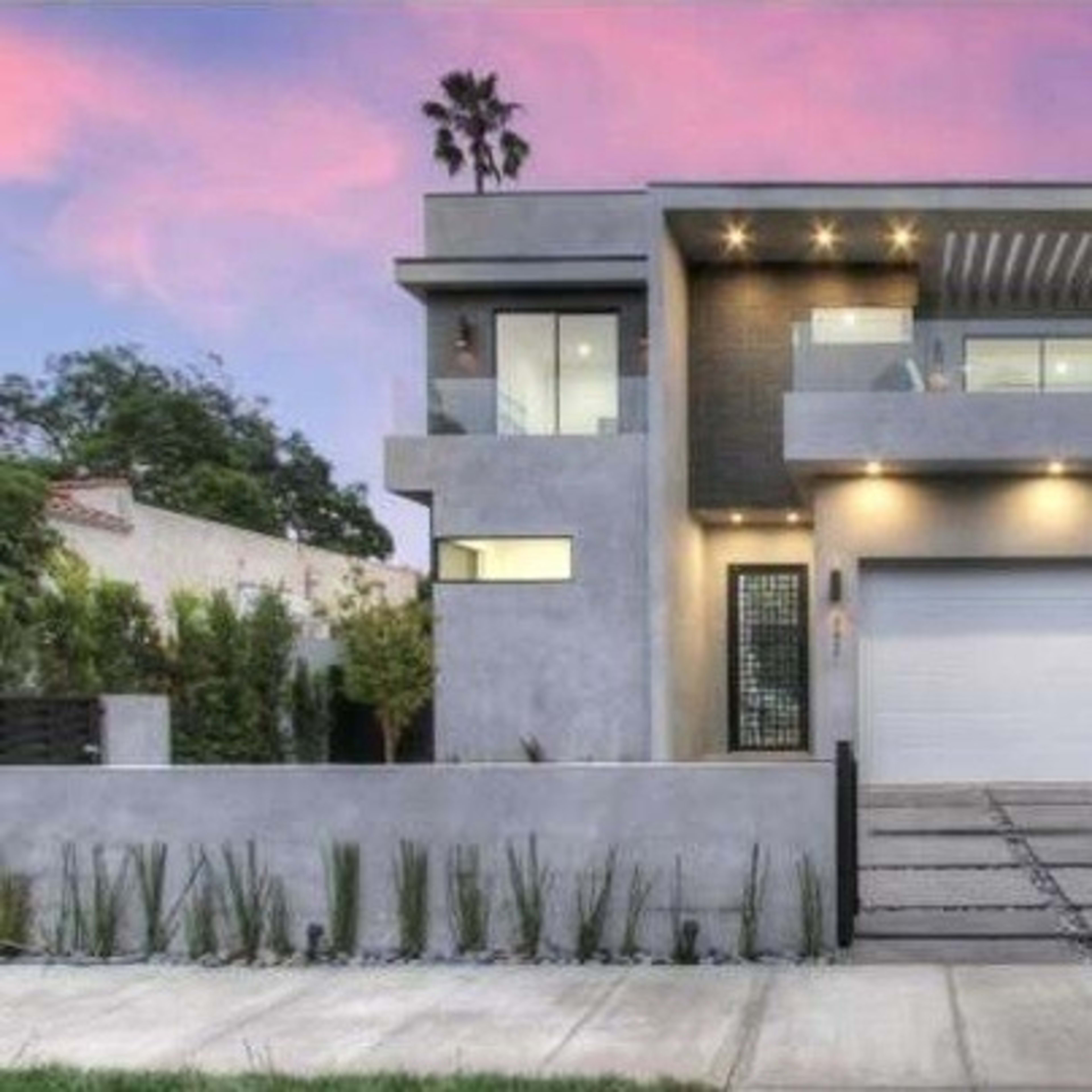 A modern two-story house with a gray exterior, large windows, and a driveway lined with stone pavers.