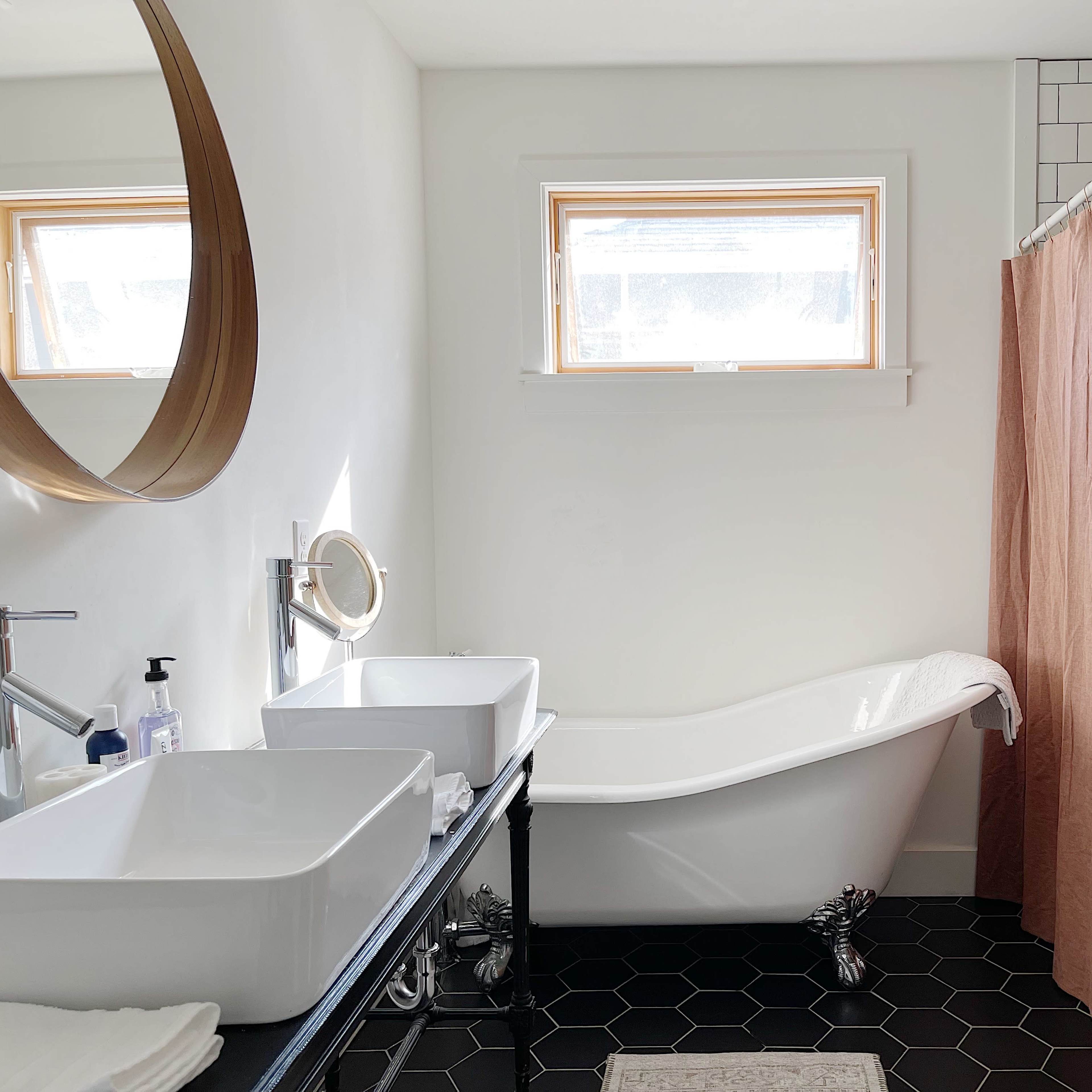 A modern bathroom featuring a freestanding bathtub, a double sink vanity, and a light-colored shower curtain.