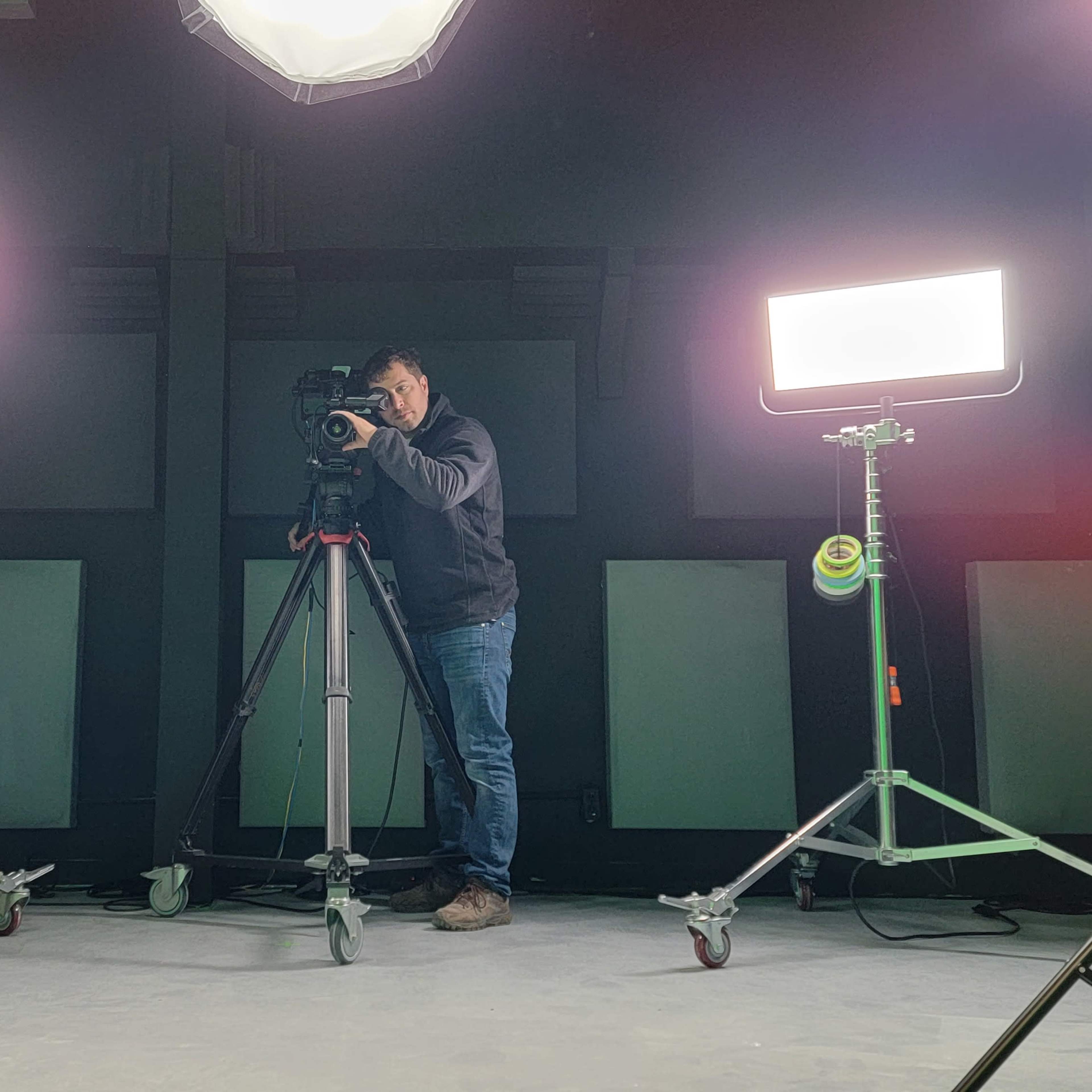 A green screen studio with lighting equipment and a camera setup on a tripod.
