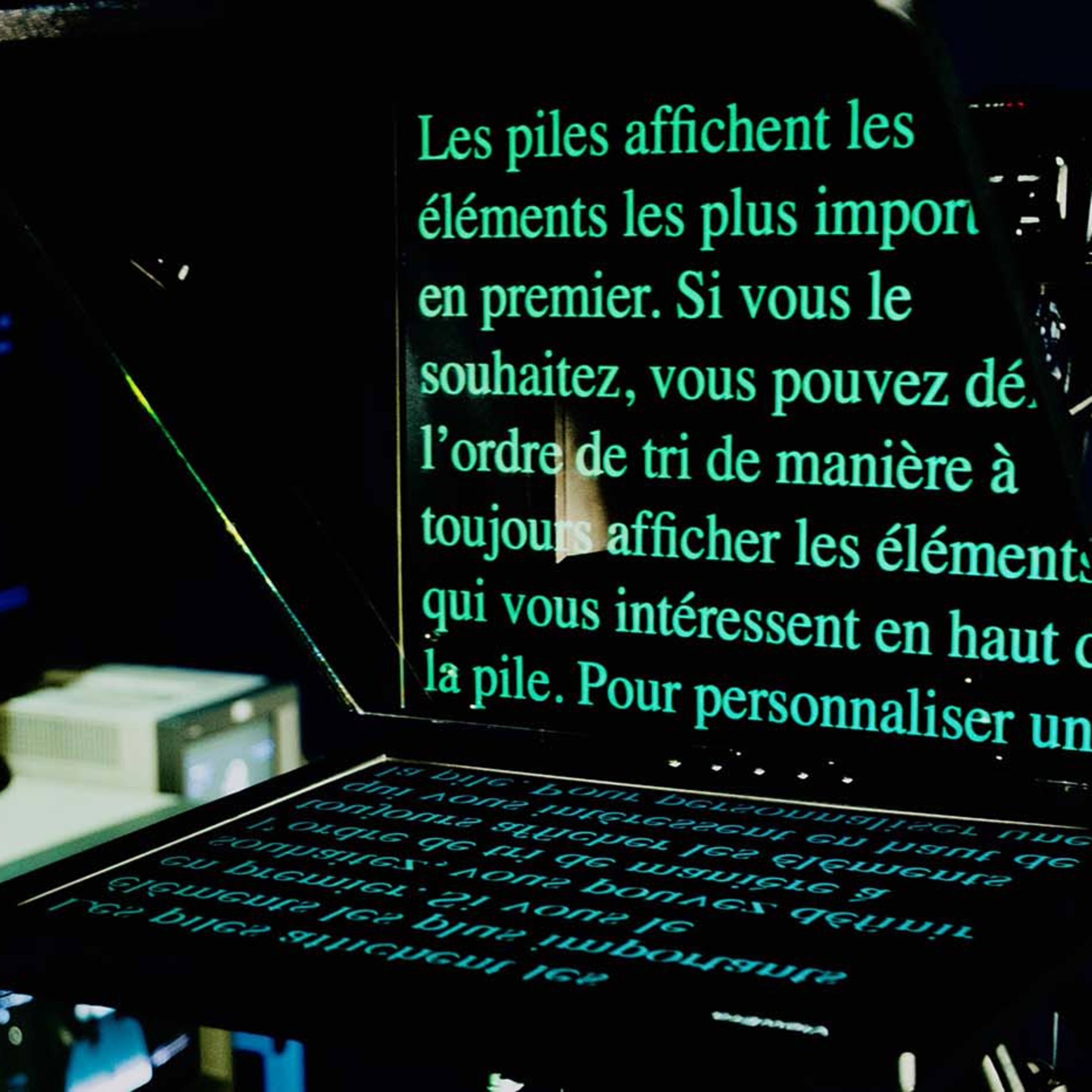 A teleprompter displaying French text, with a blurred background featuring a figure and technical equipment.