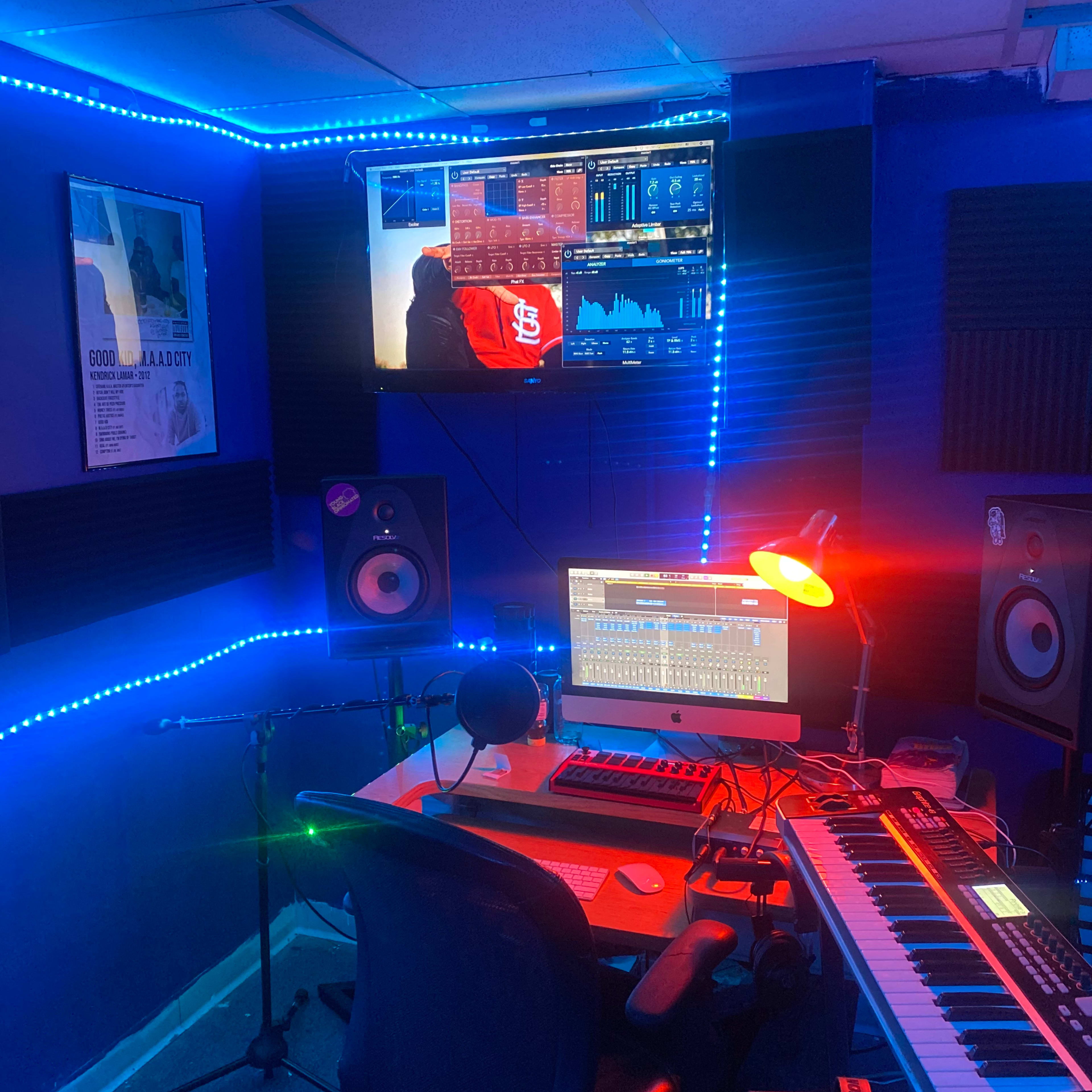 A music studio setup with a computer, keyboard, and monitors surrounded by colorful LED lights.