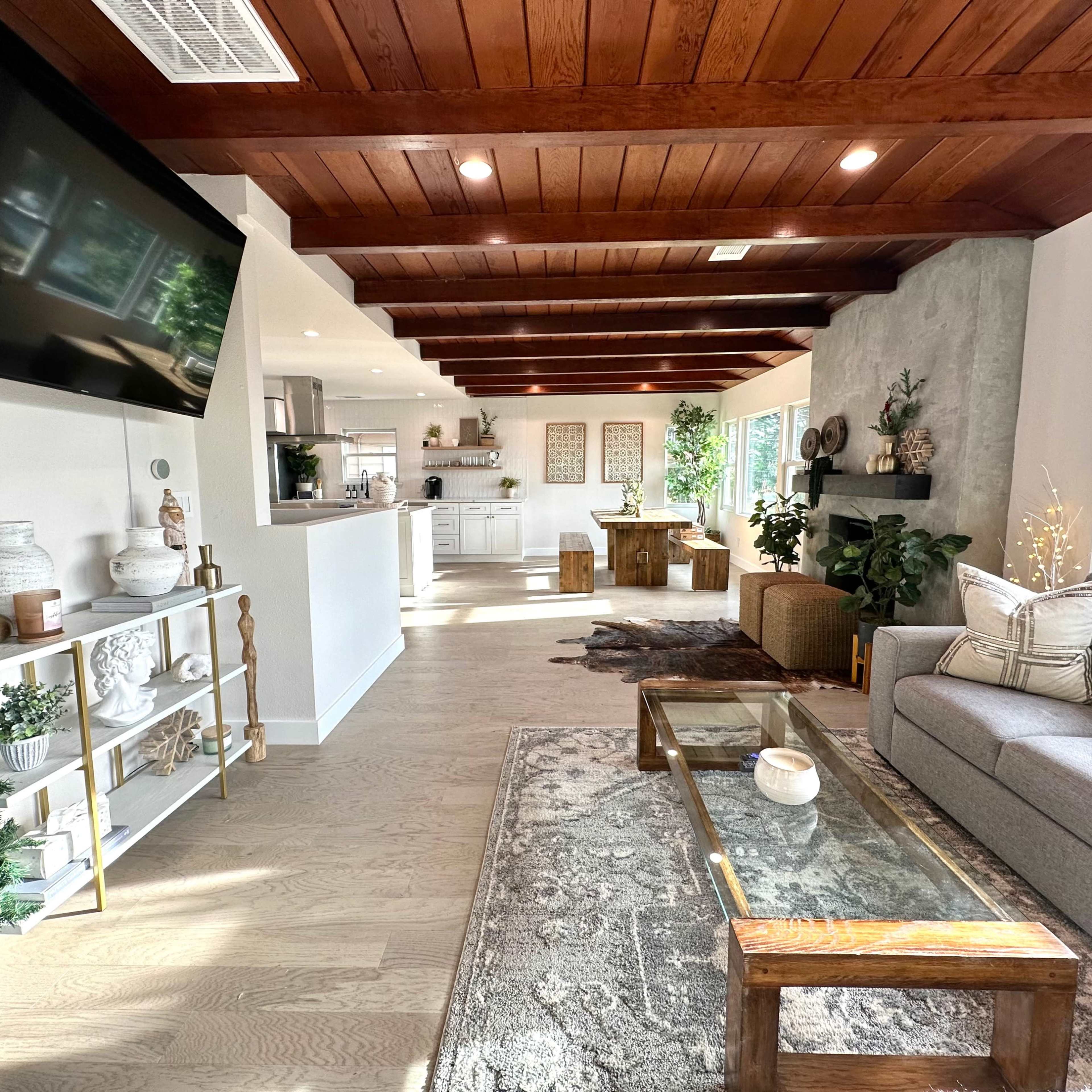 A modern living room with a gray sofa, a wooden coffee table, and an open layout featuring a kitchen area in the background, all illuminated by natural light.