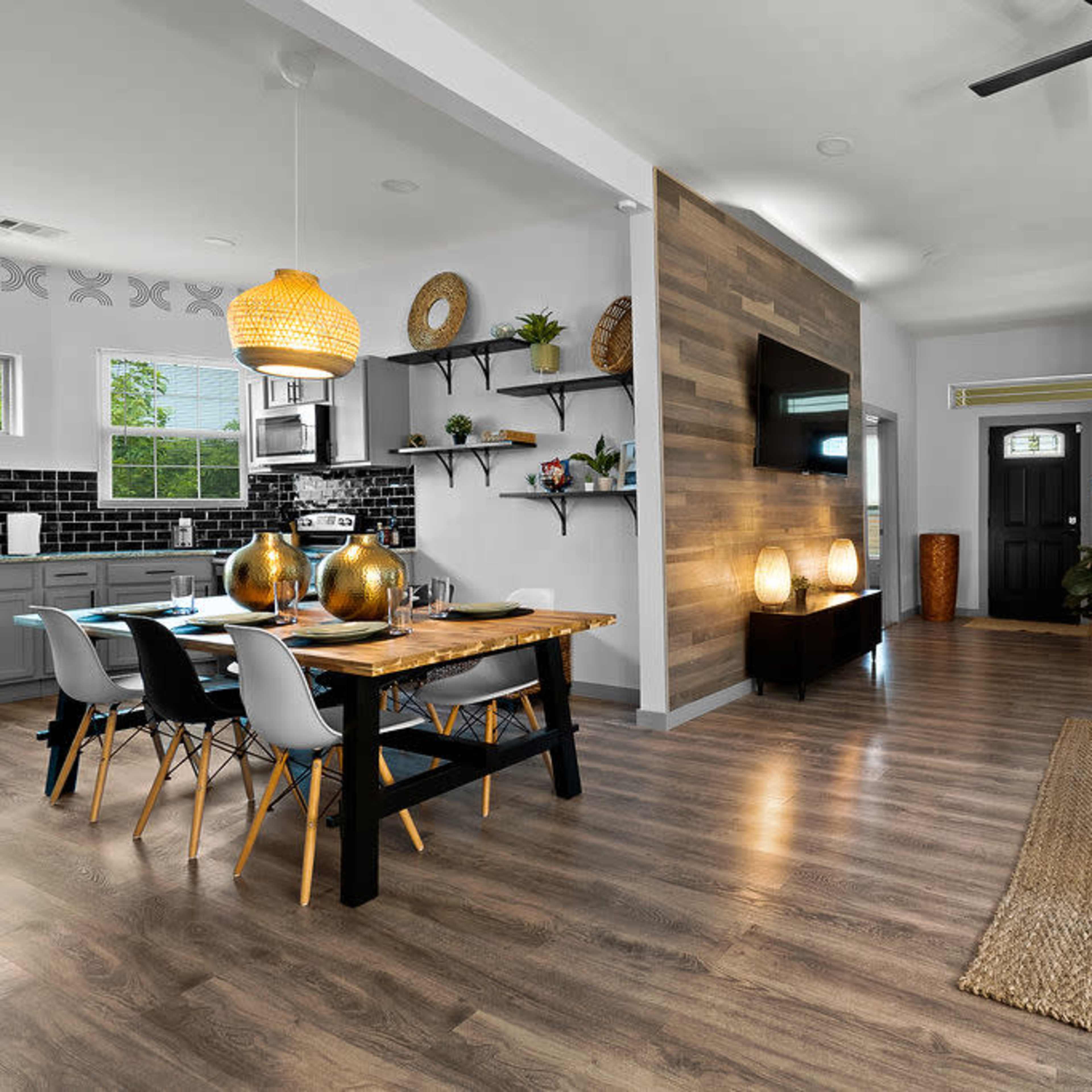 A modern open-concept living space featuring a dining area with a black table and white chairs, a kitchen with black tiles, and a cozy lounge area with a sofa and coffee table.