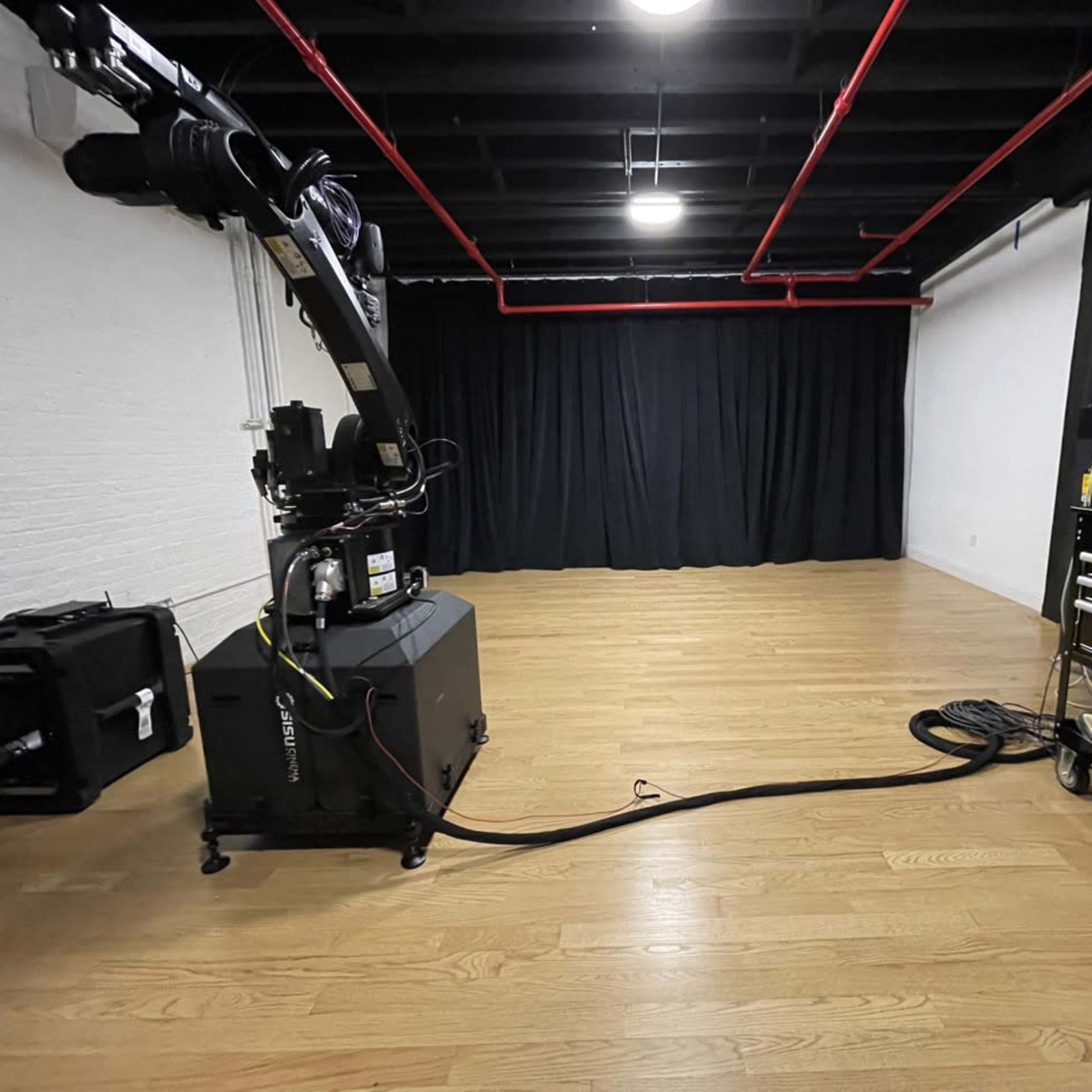 A spacious studio with wooden flooring, a black curtain backdrop, and a camera on a movable rig positioned to the left.