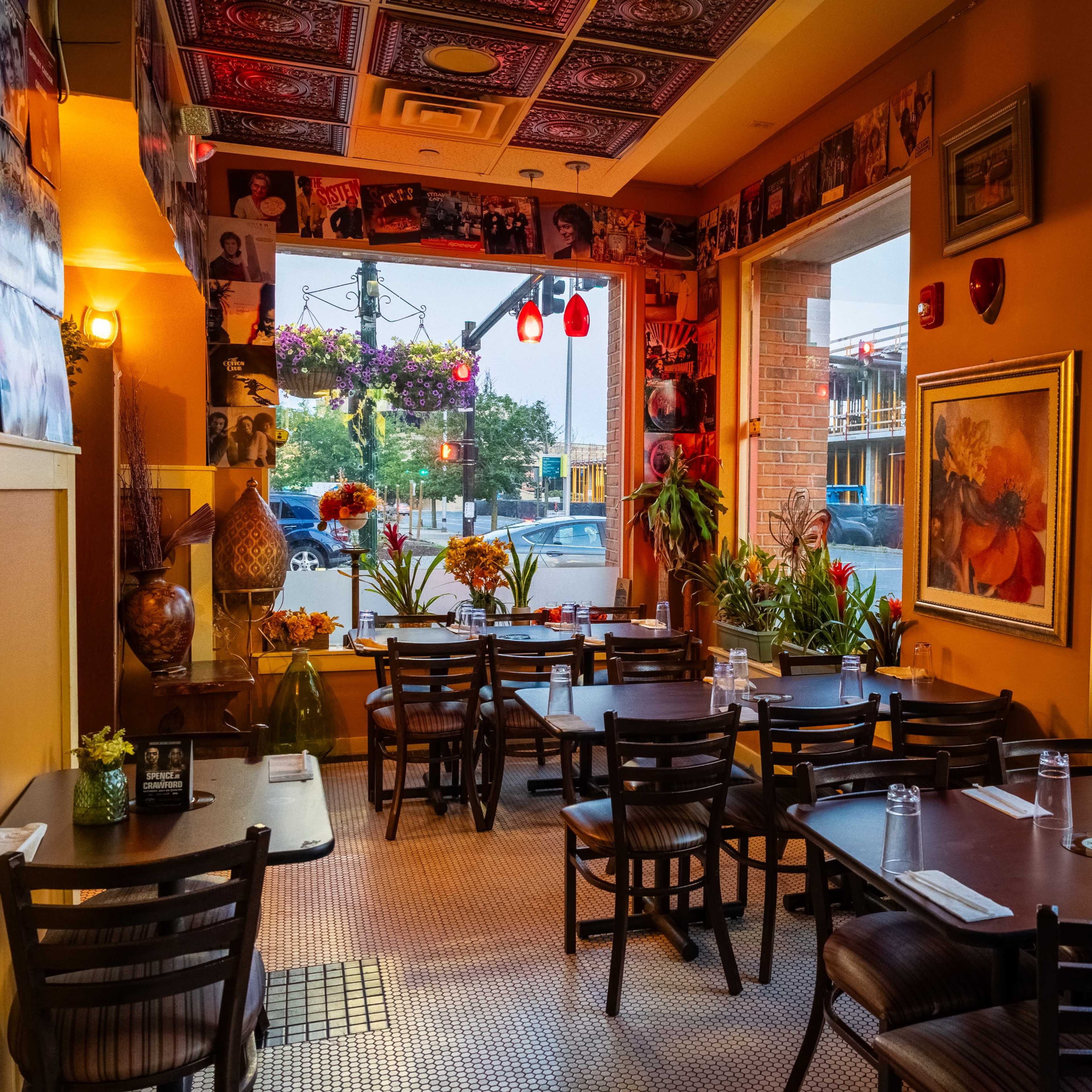 The interior of a restaurant with tables set for dining, decorated with plants and colorful wall art.