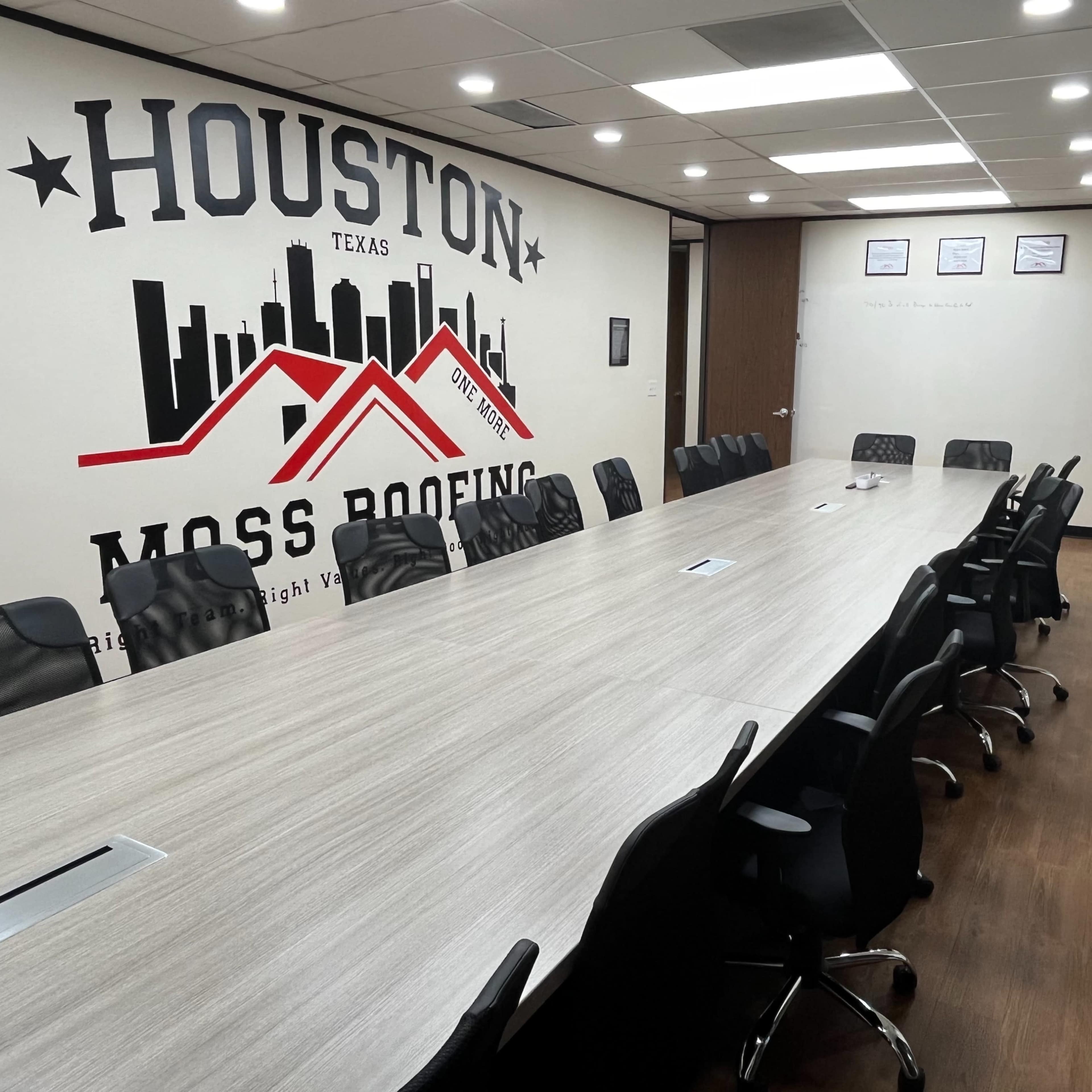 A modern conference room with a long, rectangular table surrounded by black chairs and a wall featuring a mural of the Houston skyline and company branding.