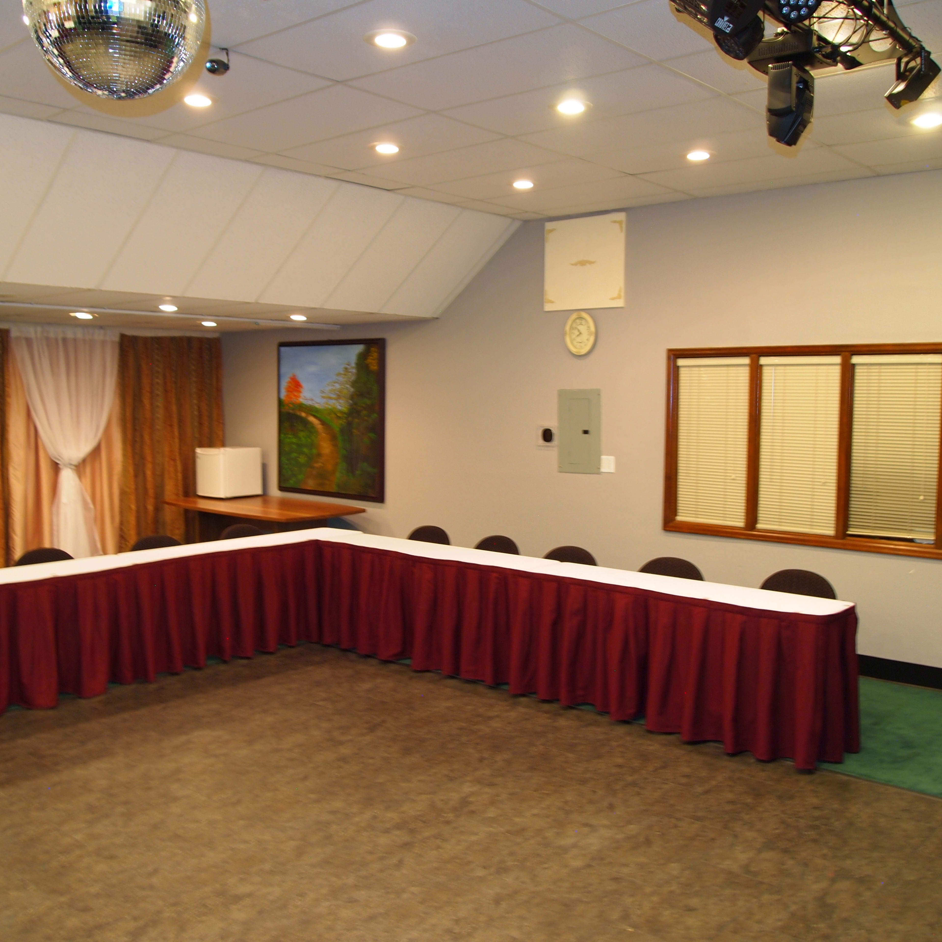 A conference room features a long table surrounded by chairs, with a disco ball hanging from the ceiling and a painting on the wall.